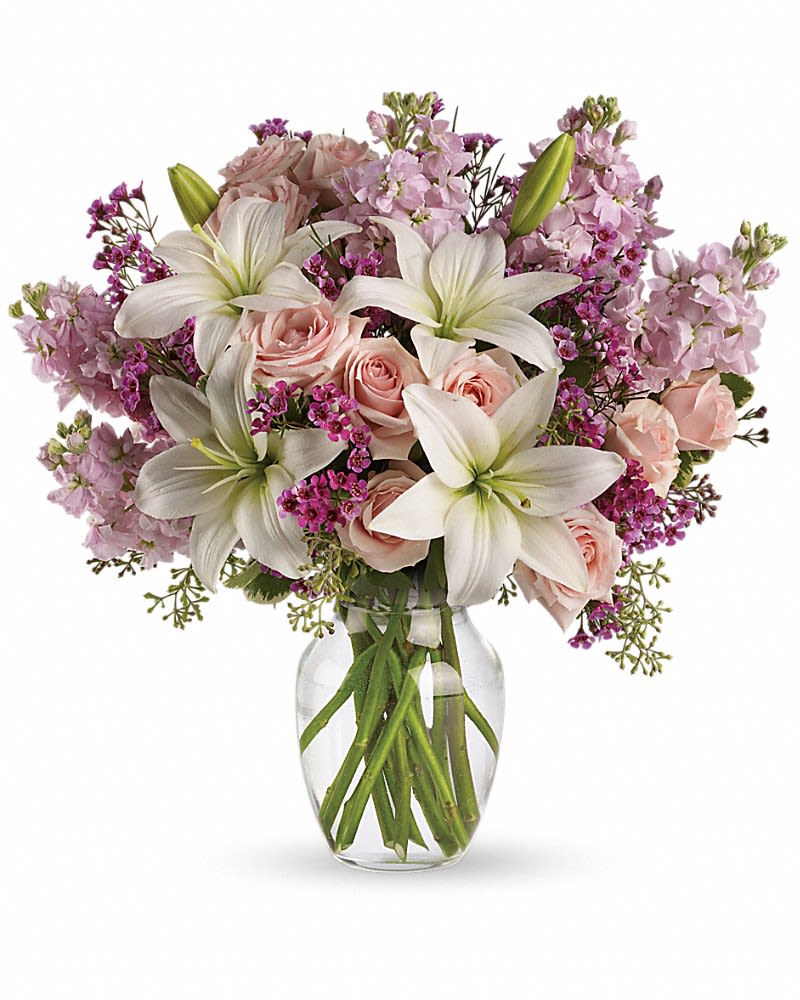 Arrangement of white lilies, pale pink roses and purple flowers in a clear glass vase