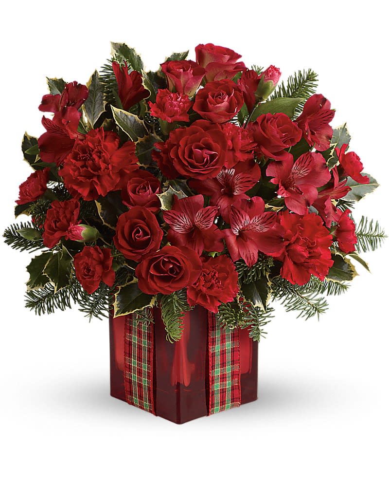 Red roses and carnations in a red cube vase with plaid ribbon and holiday evergreens