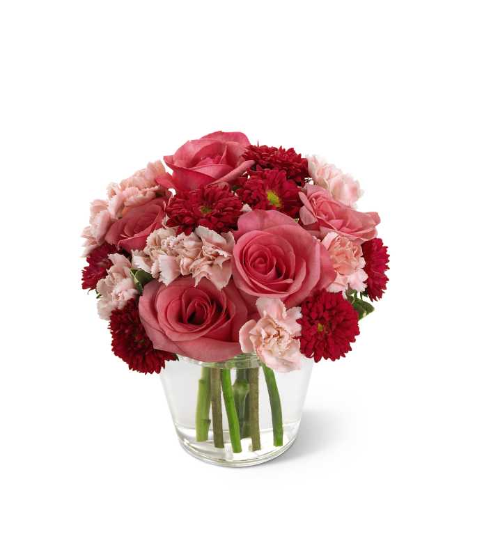 Short arrangement of pink roses, pale carnations, and red mums in a clear glass vase
