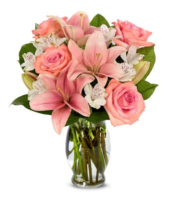 Pink lilies, roses, and white alstroemeria arranged in a clear glass vase
