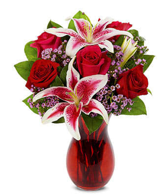 Red roses and pink lilies with purple filler flowers in a red glass vase