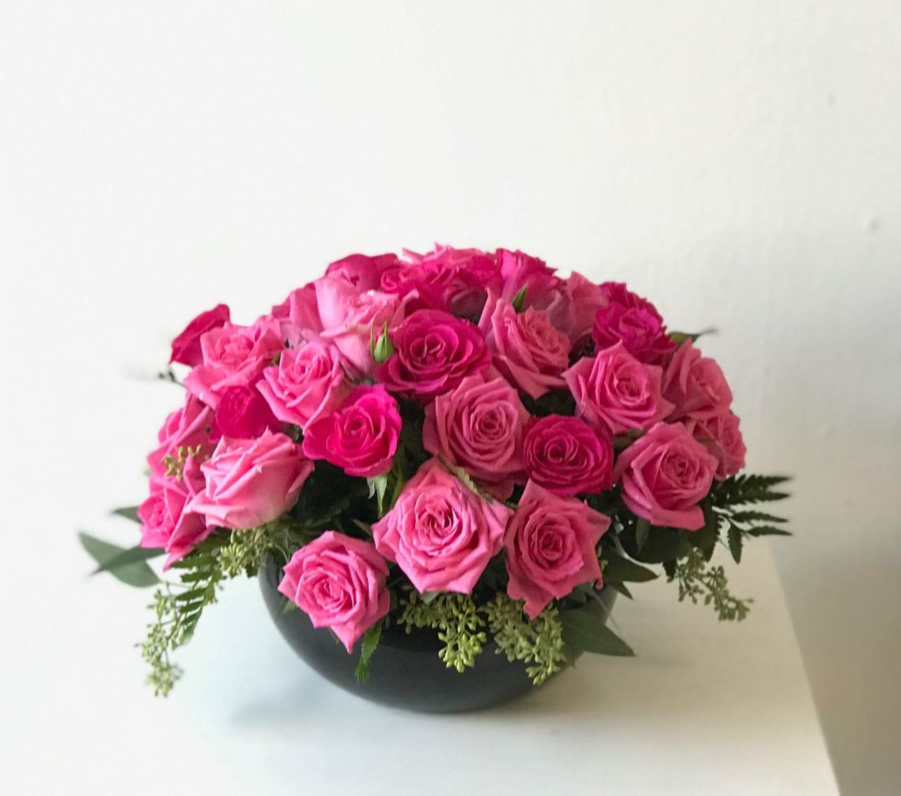 Low round arrangement of hot pink roses in a black bowl-shaped vase