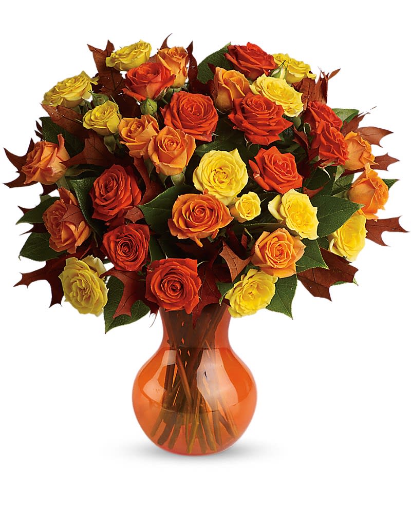 Arrangement of orange and yellow roses with fall leaves in an orange glass vase