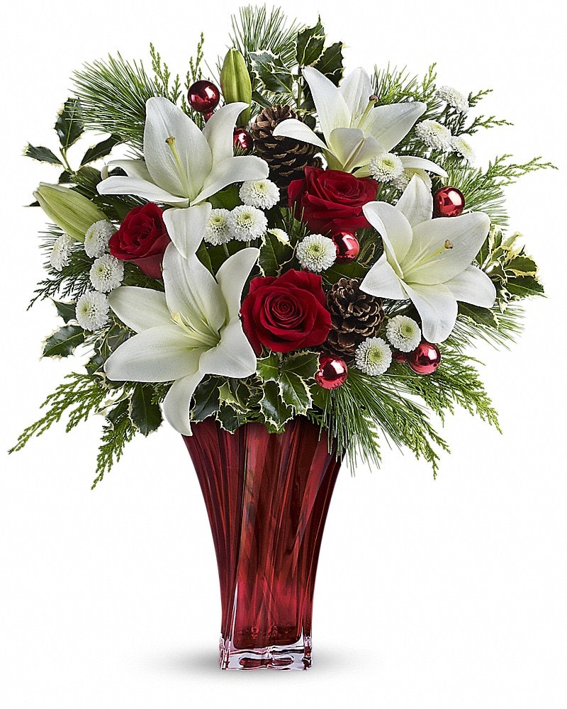 White lilies and red roses with evergreens and ornaments in a tall red glass vase
