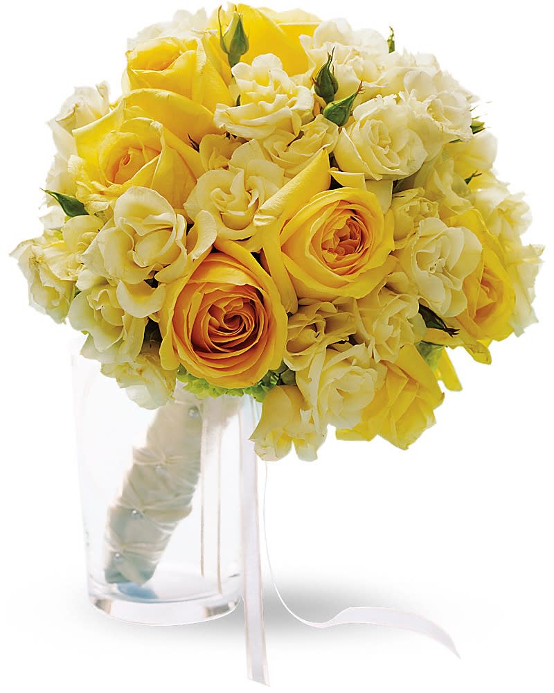 Round bouquet of yellow and cream roses with wrapped handle resting in a clear glass vase