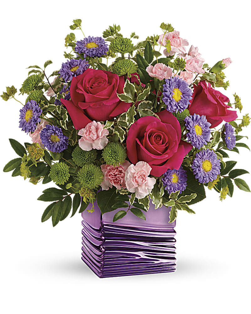 Bright bouquet of hot pink roses, purple asters, and pink carnations in a shiny purple cube vase