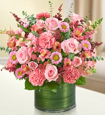 Pink roses, carnations, and mixed flowers in a short green-wrapped glass cylinder vase