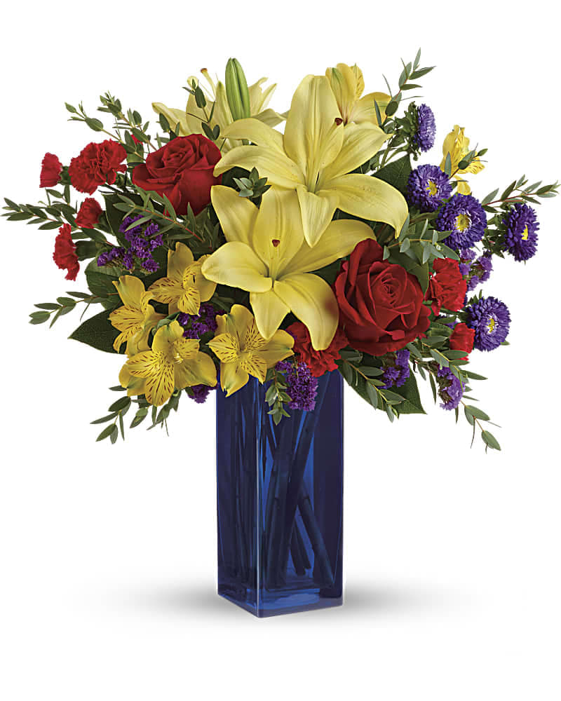 Tall blue vase with yellow lilies, red roses, red carnations, and purple and yellow accent flowers