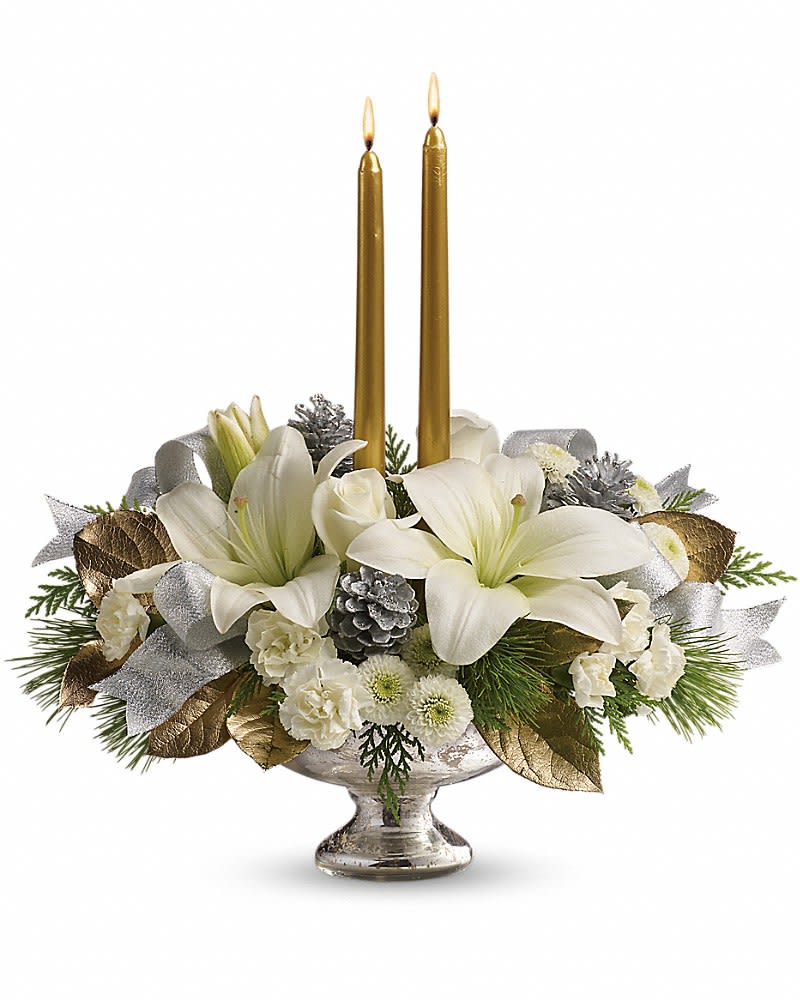 Low centerpiece of white lilies and other white flowers with two gold taper candles in a silver bowl.