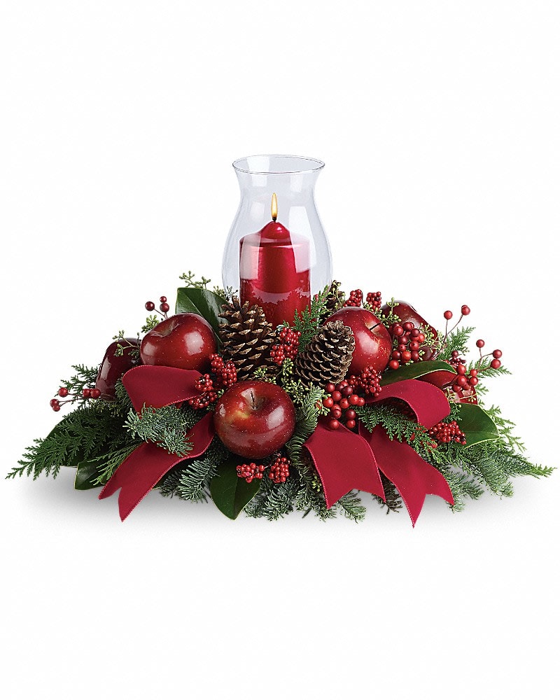 Holiday centerpiece with red candle in glass holder, red apples, berries, pinecones, and evergreen branches.