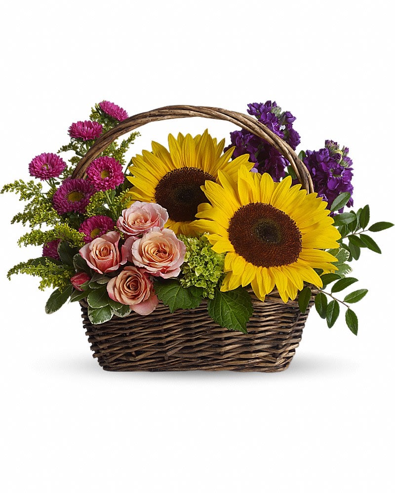 Wicker basket arrangement with sunflowers, pink roses, and purple flowers.