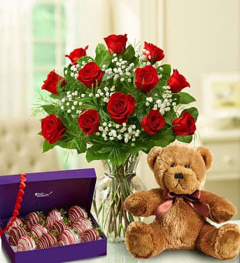 Red rose bouquet in a glass vase with a teddy bear and box of chocolate-covered strawberries