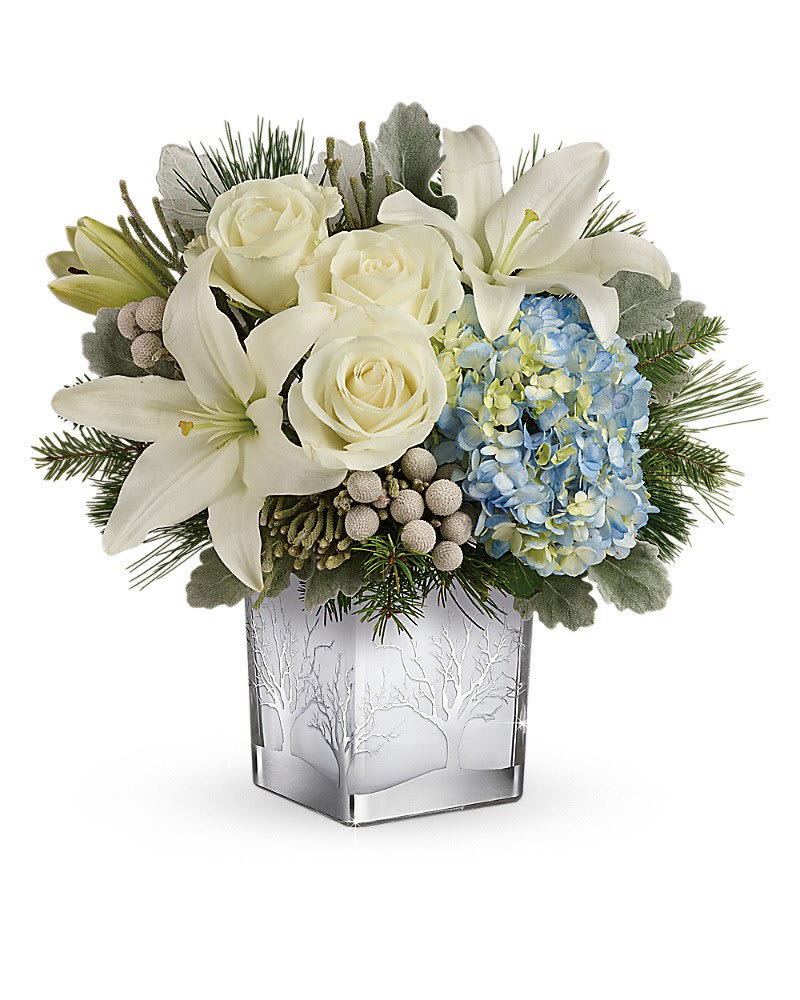 Compact arrangement of white lilies and roses with blue hydrangea in a frosted cube vase.