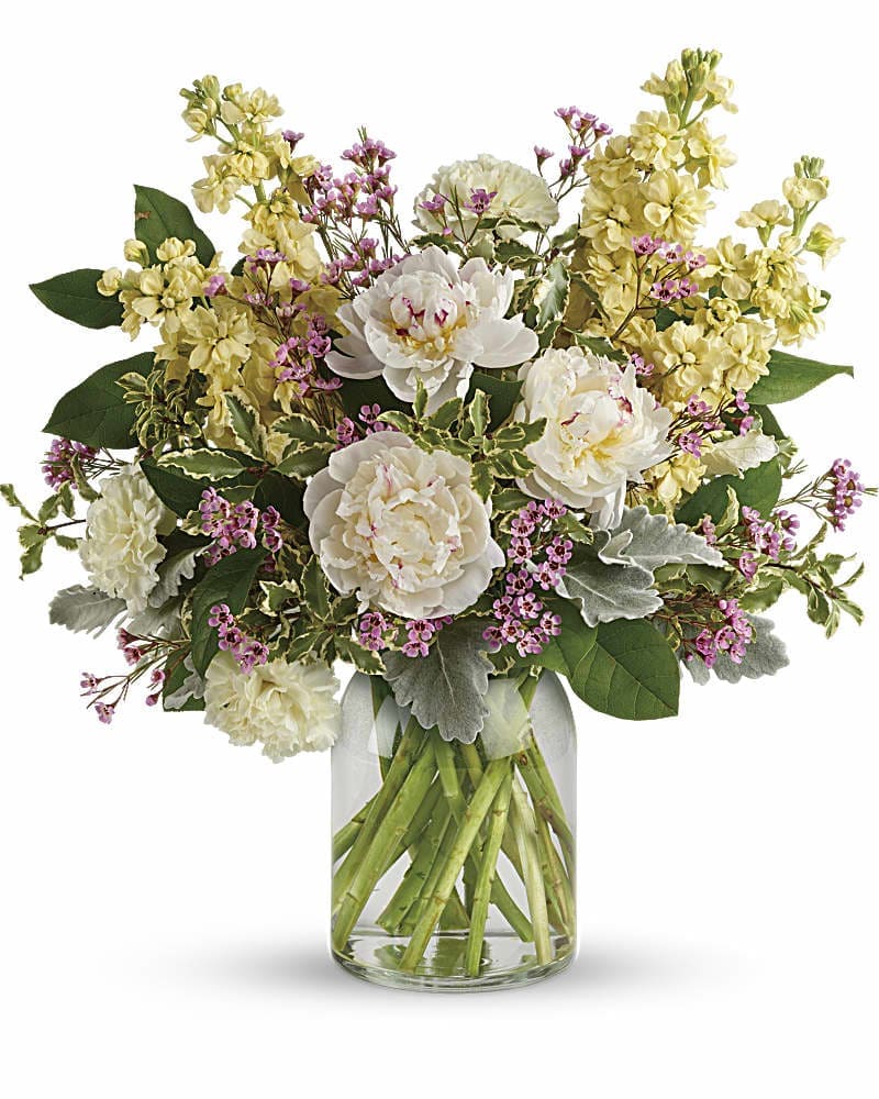 Arrangement of white peonies, yellow stock, and pink filler flowers in a clear glass jar vase