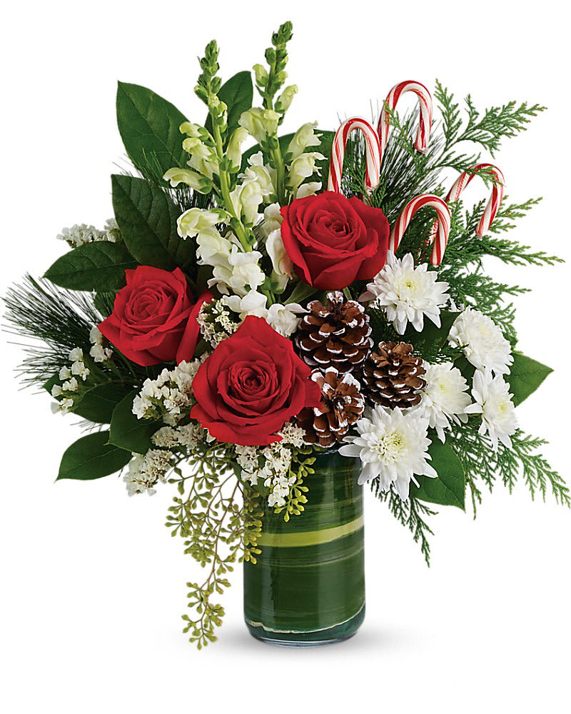 Christmas arrangement with red roses, white flowers, pinecones, and candy canes in a green-wrapped glass vase
