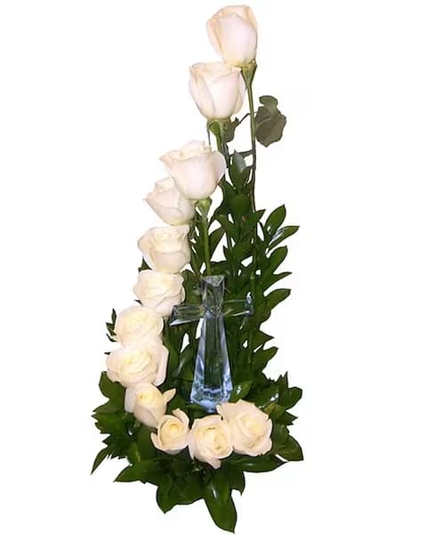 White roses arranged around a clear glass cross with greenery