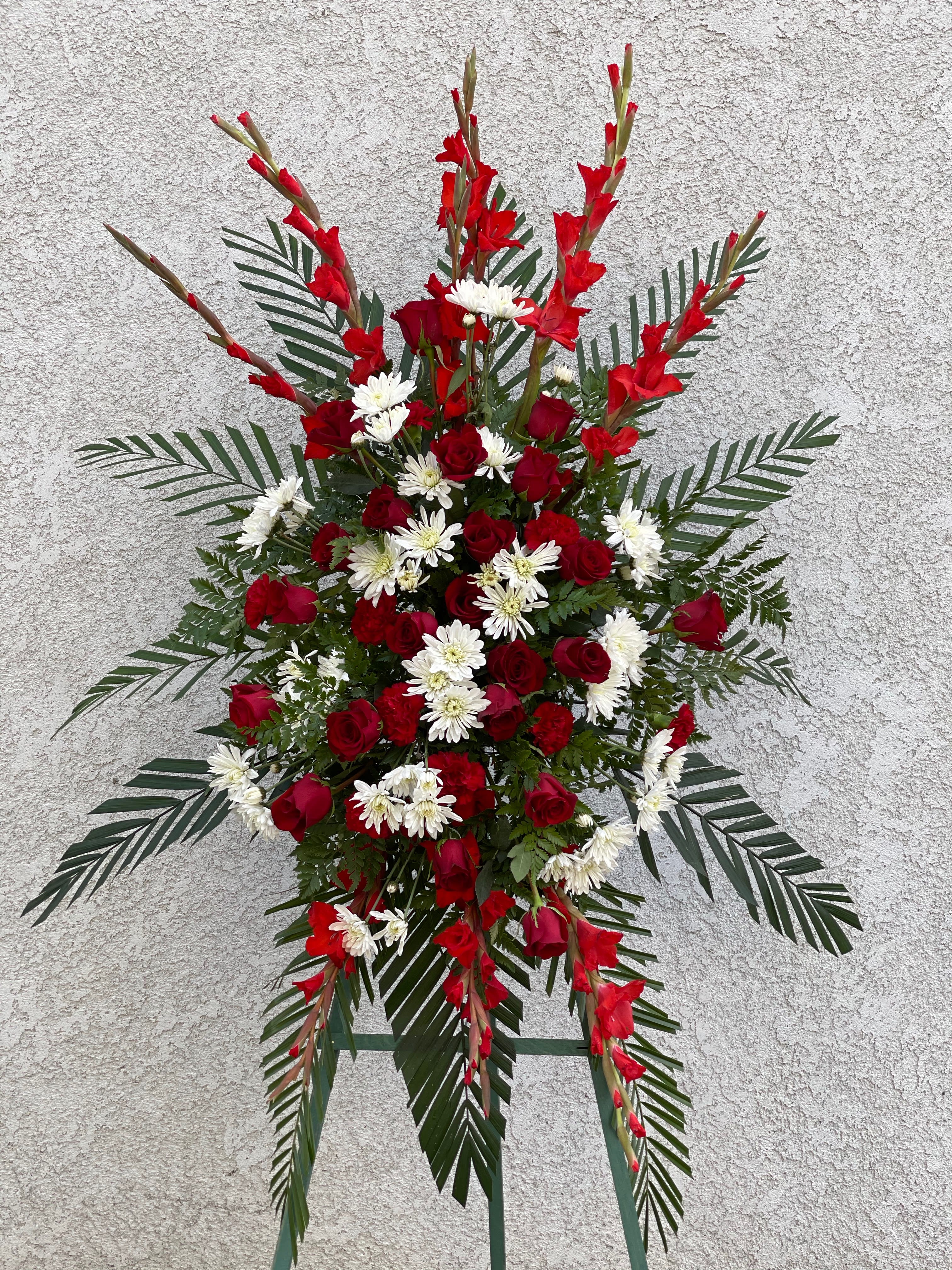 Standing floral spray with red roses and white daisies on a metal easel