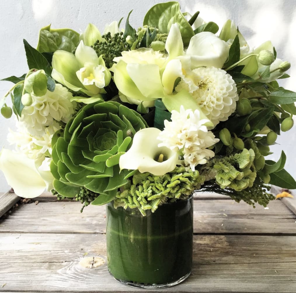 Green and white floral arrangement in a dark glass vase
