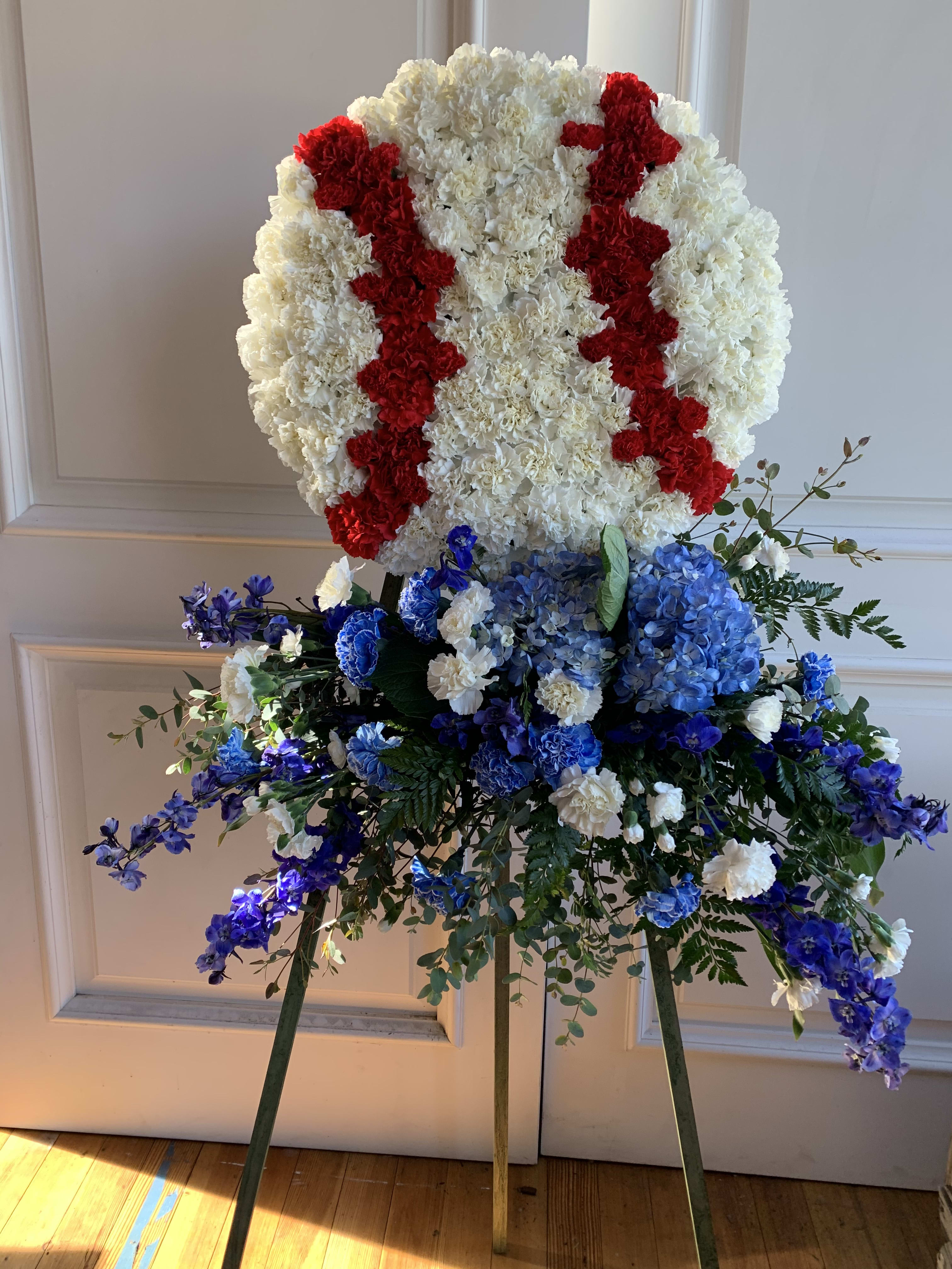 Large standing floral tribute with white, red, and blue flowers on an easel