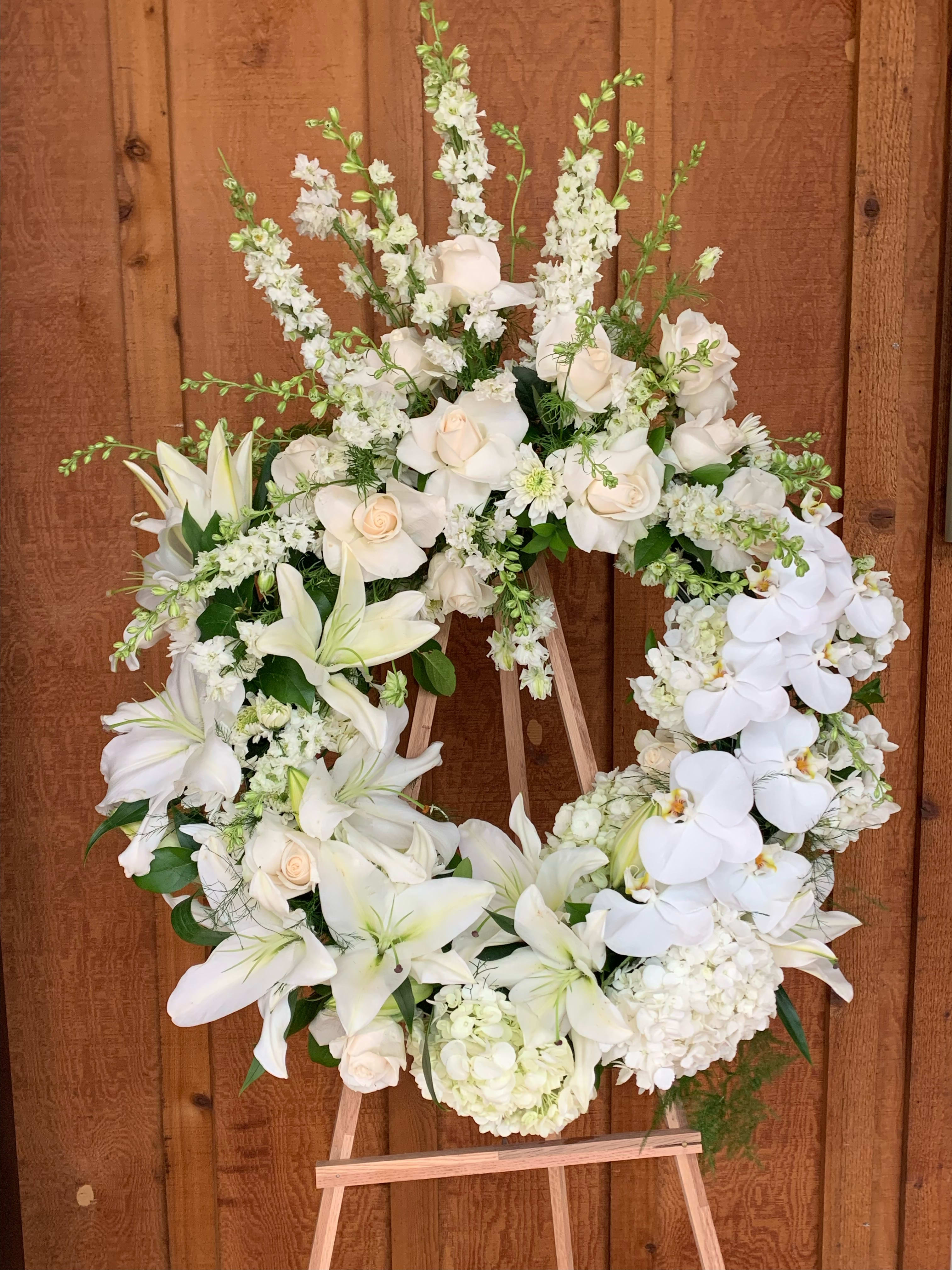 White floral wreath on a wooden easel with lilies, roses, and orchids