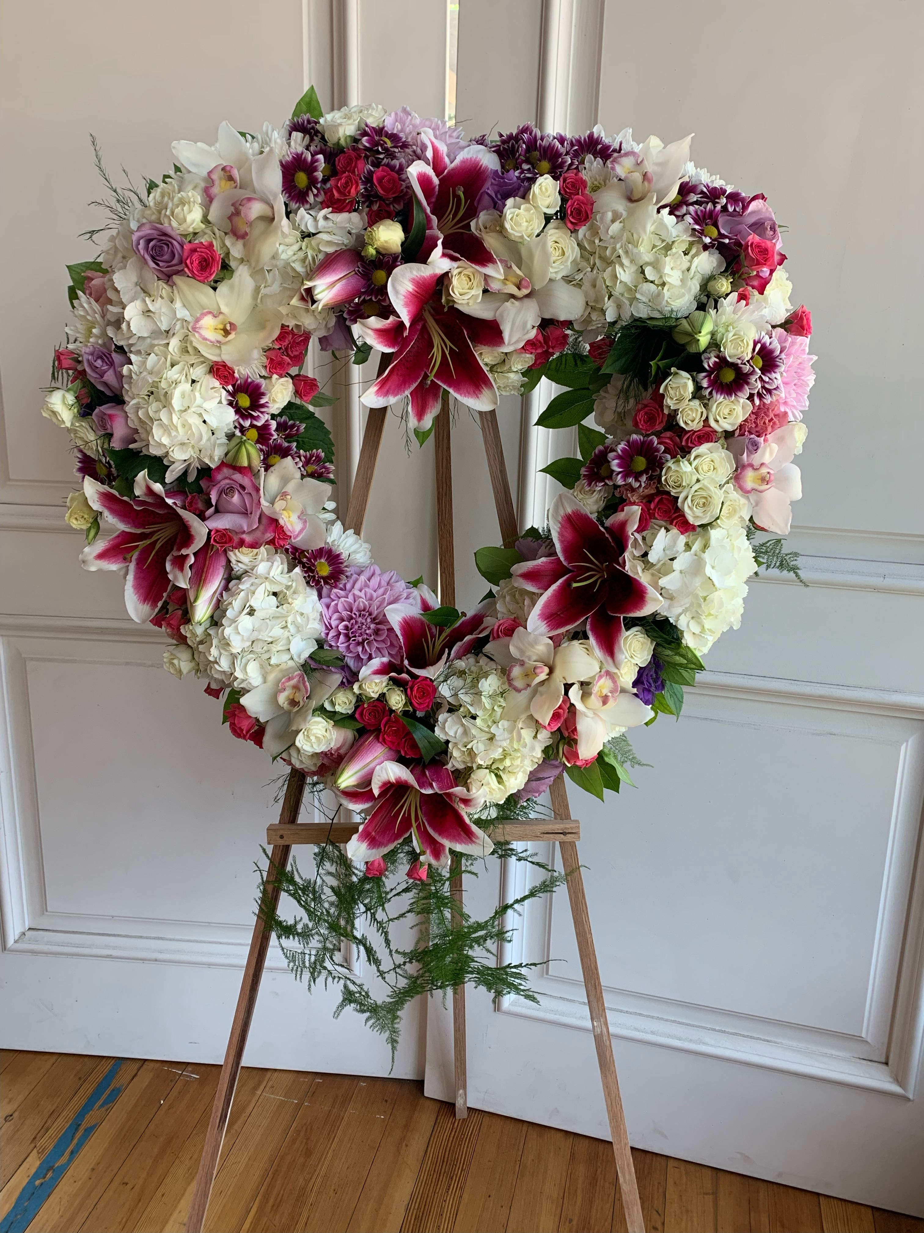 Heart-shaped floral wreath on a wooden easel with pink, white, and purple blooms