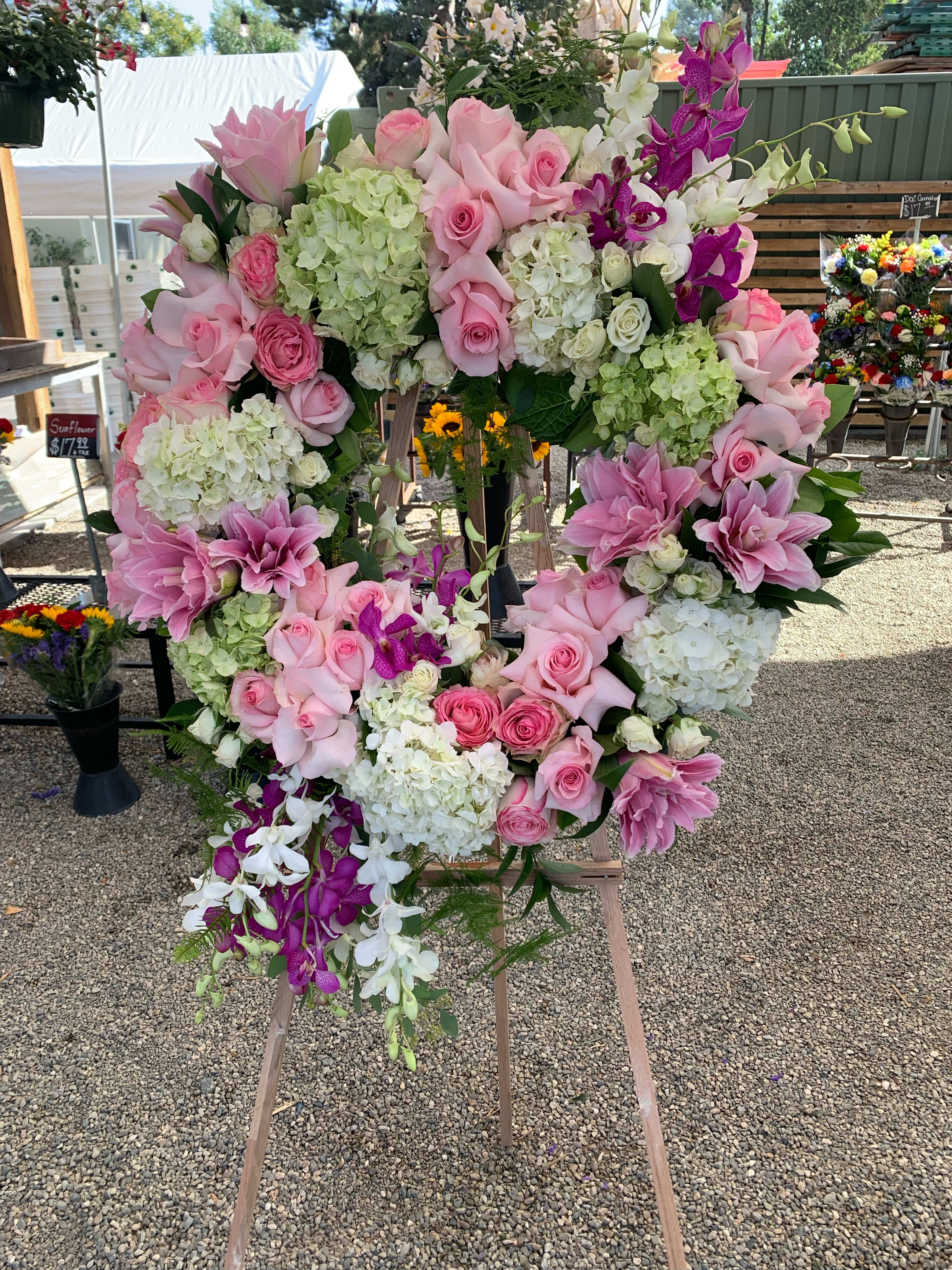 Large floral wreath of pink roses, hydrangeas, lilies, and orchids on an easel