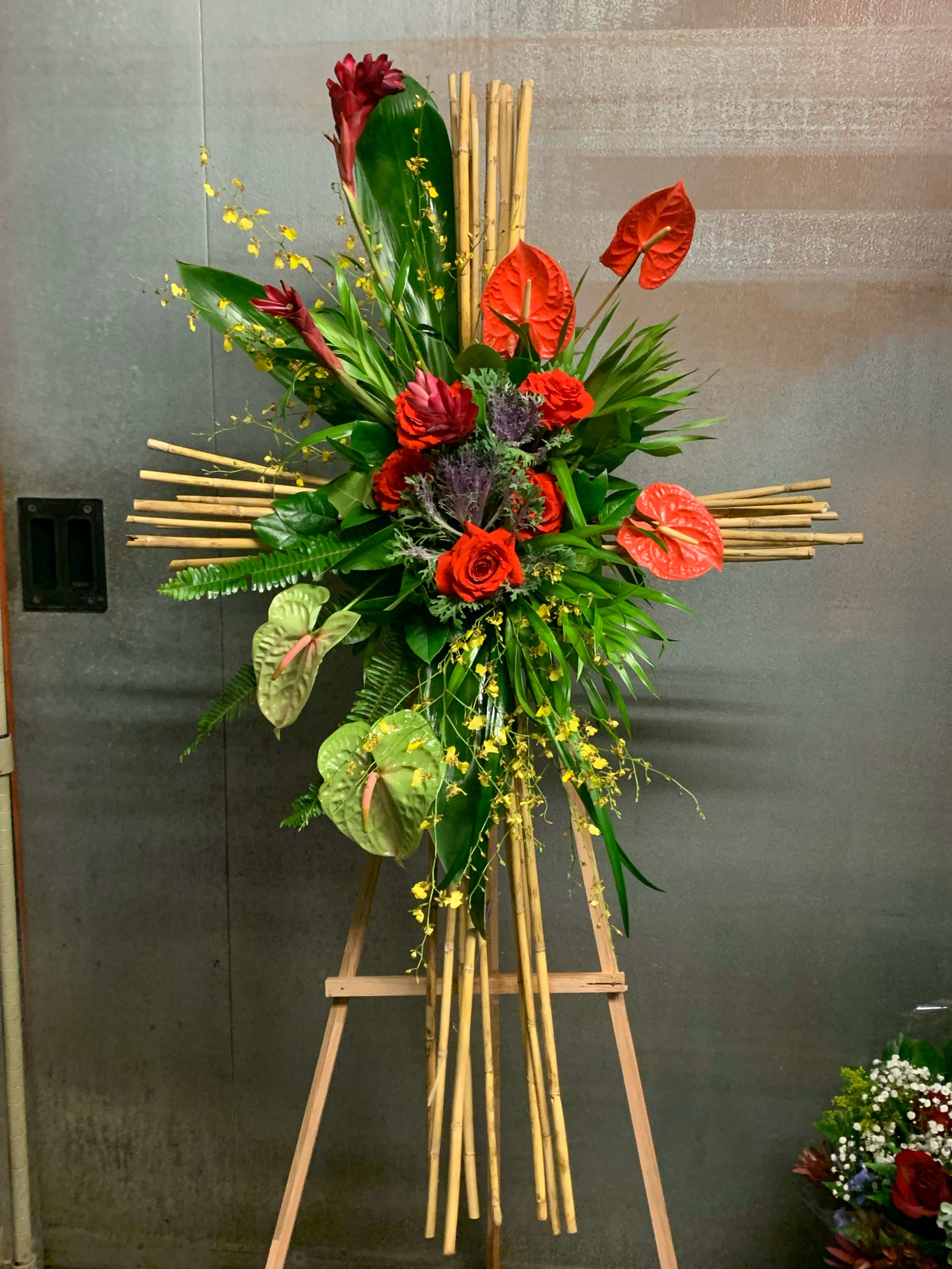 Tall tropical floral arrangement with red anthuriums and roses on a bamboo stand