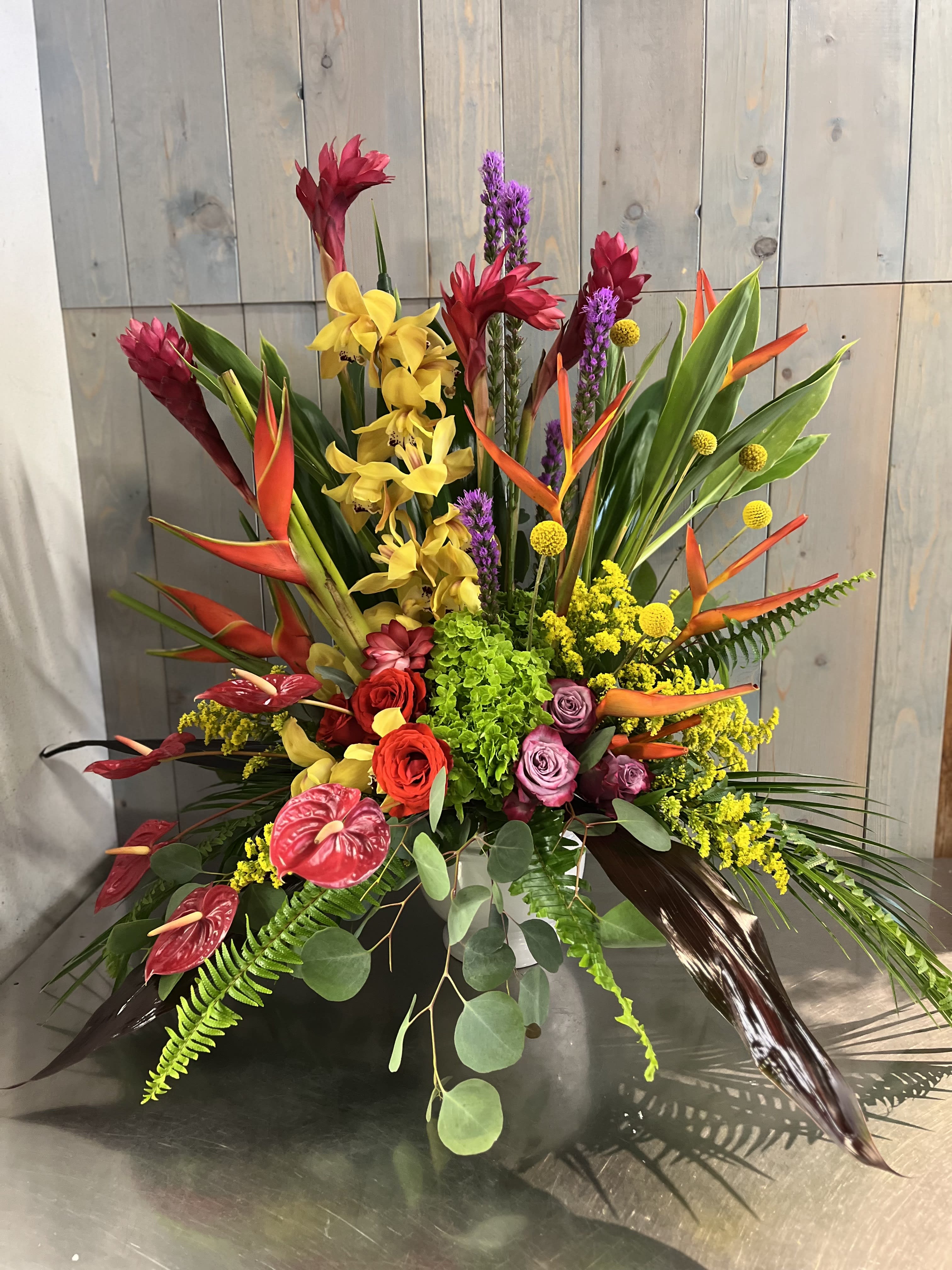 Tropical floral arrangement with orchids, roses, and bird-of-paradise in a low container