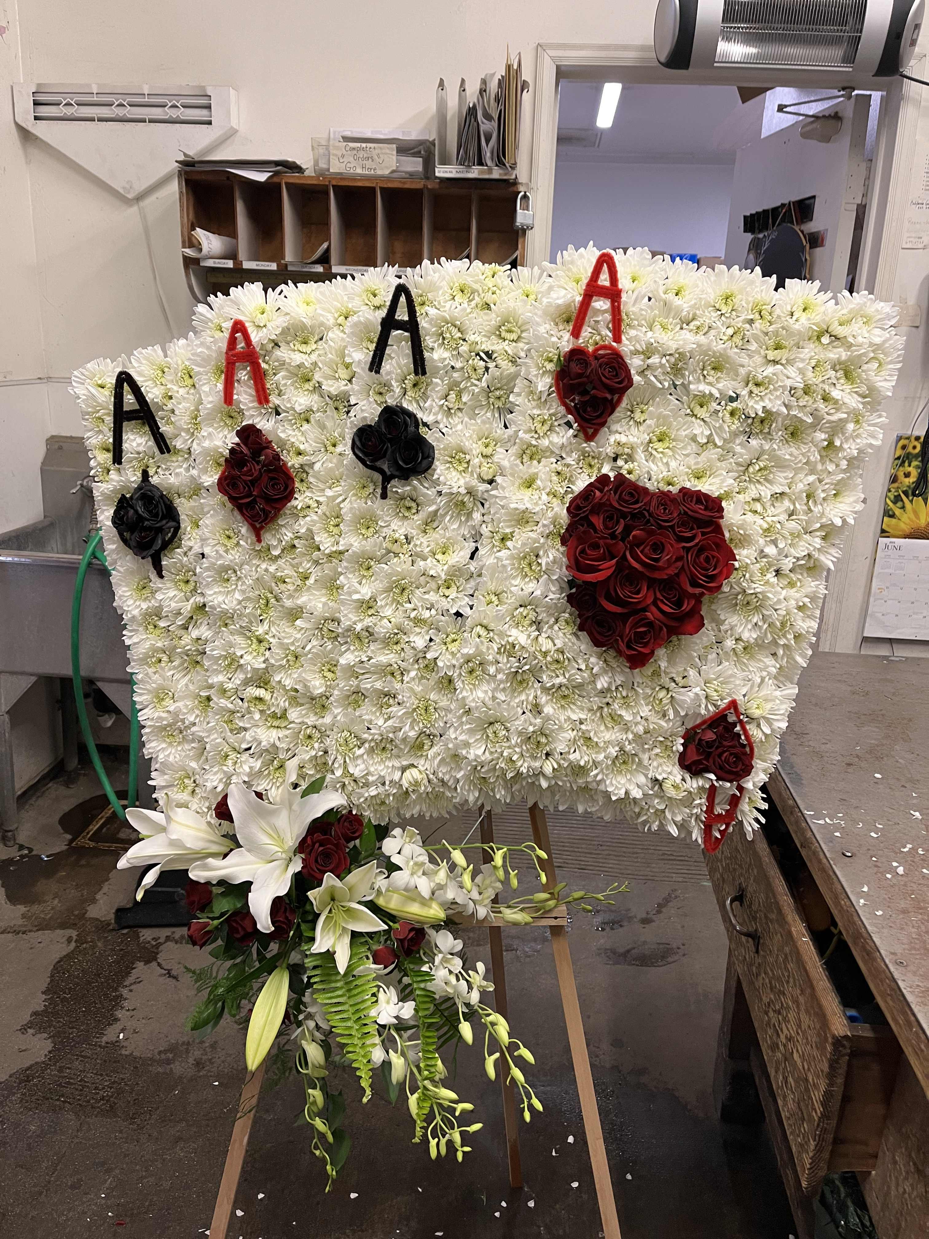 Large floral tribute board with white chrysanthemums, red roses, and lilies