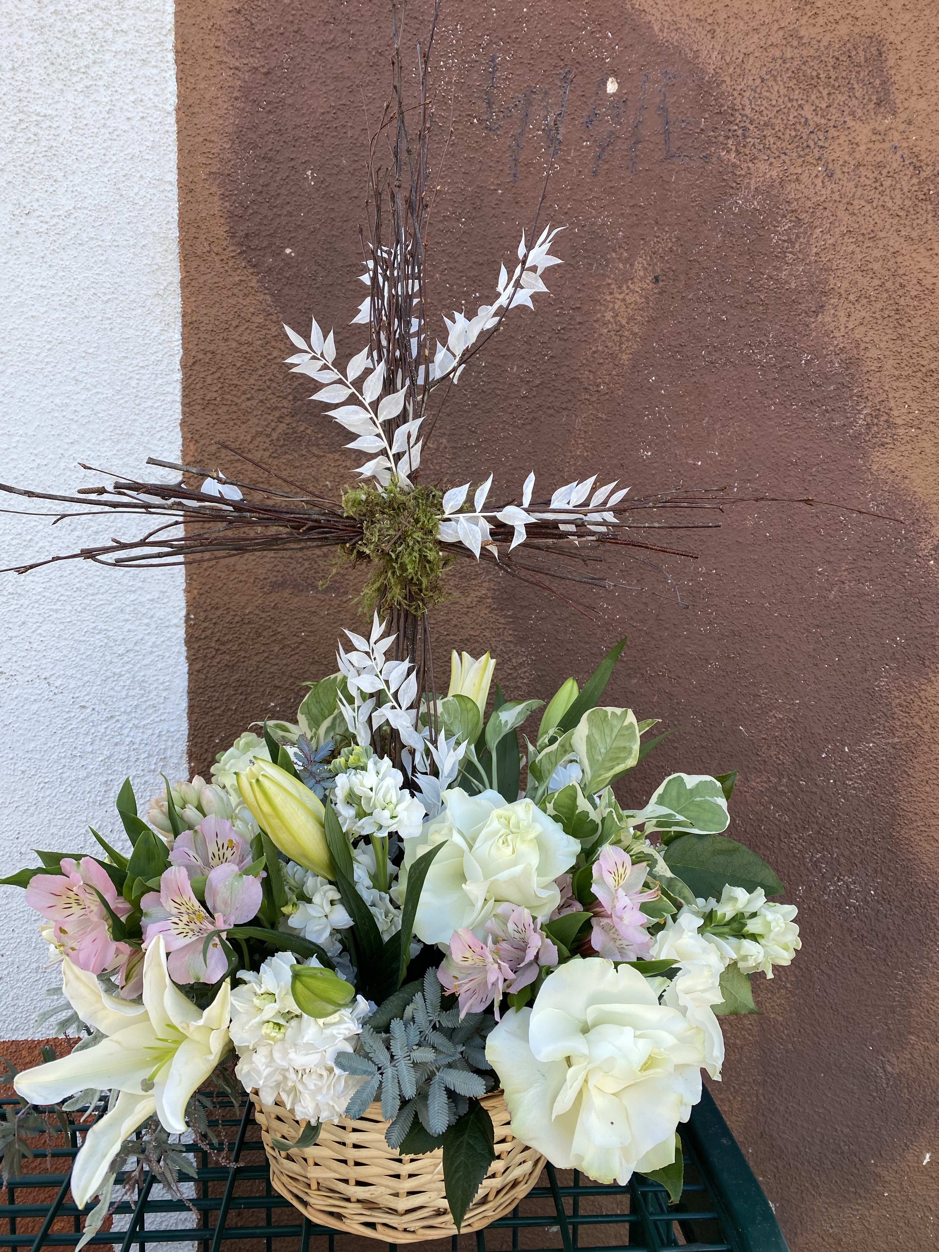 White and pale pink floral arrangement in a wicker basket with a tall cross centerpiece