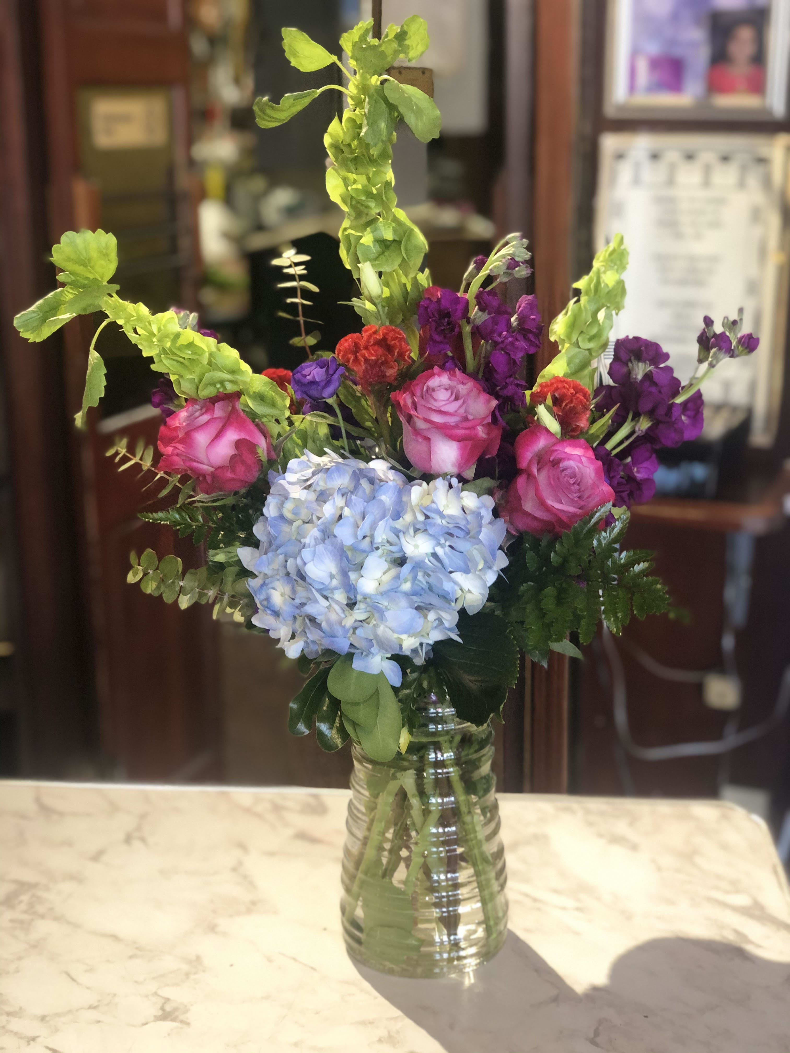 Mixed bouquet with pink roses, blue hydrangea, and purple flowers in a glass vase