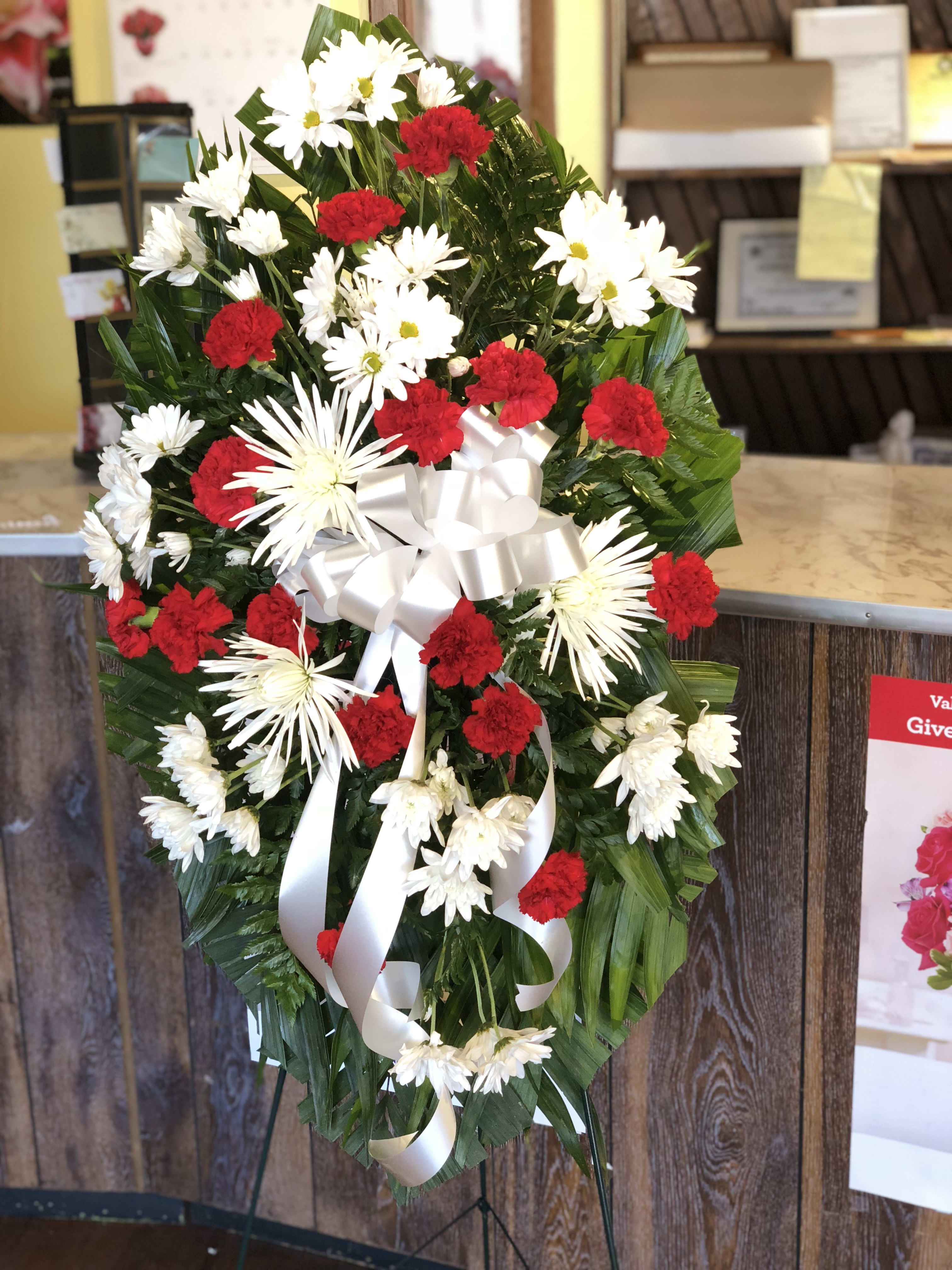 Standing floral wreath with red carnations and white daisies, tied with a white ribbon