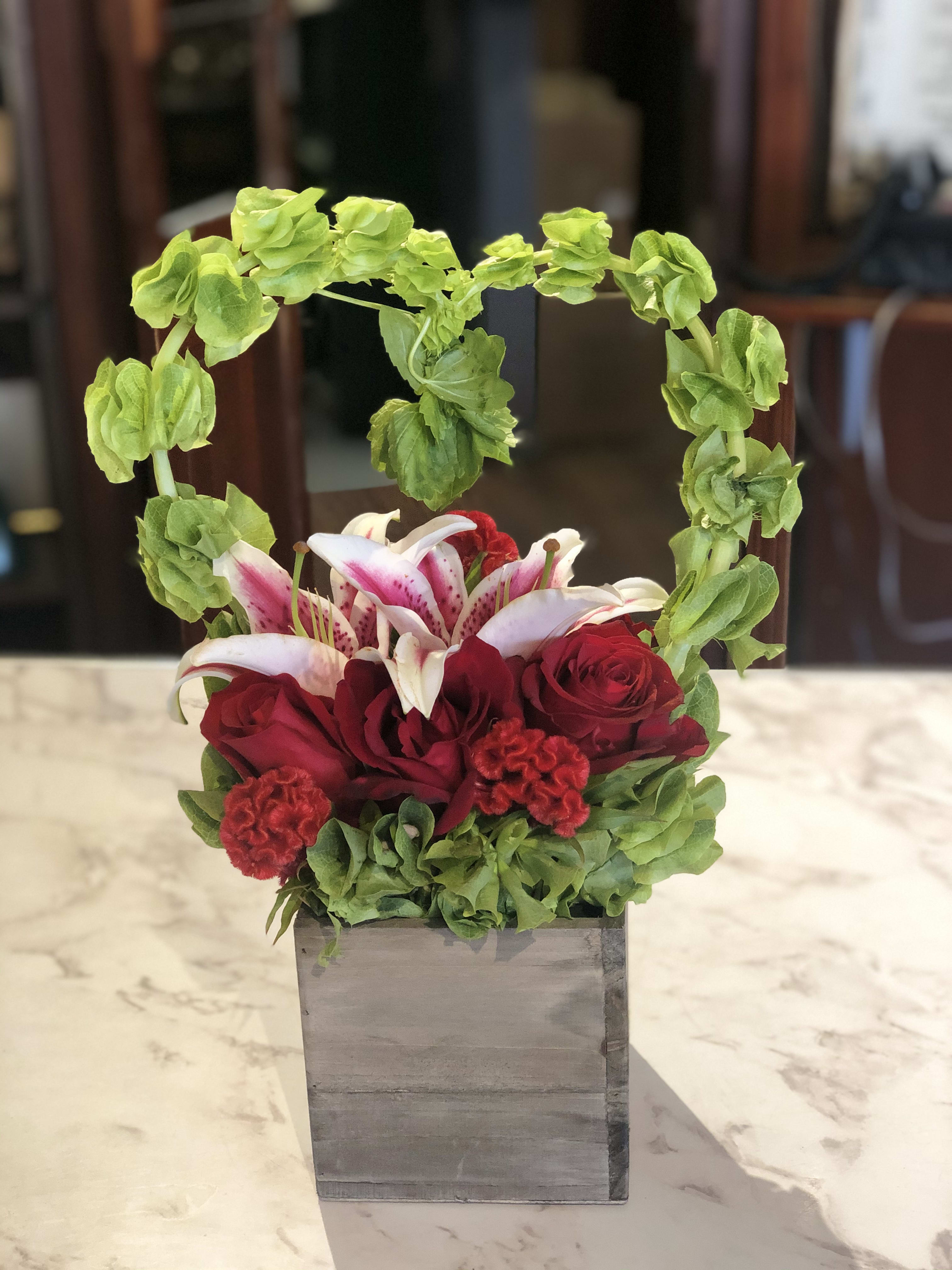 Red roses and pink lilies in a gray square vase with a green floral arch