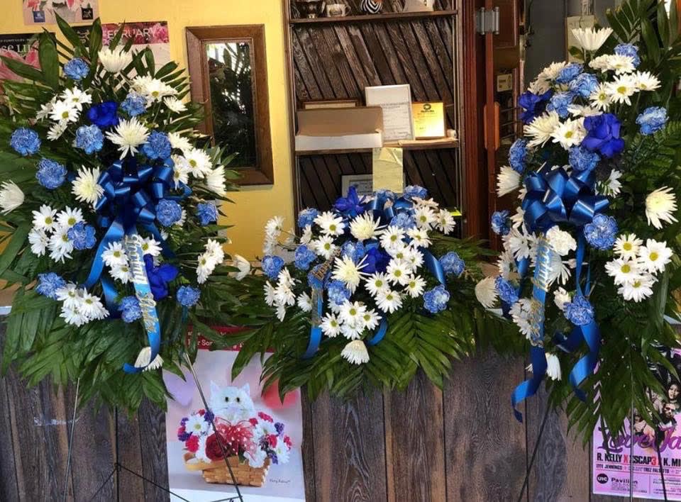 Three blue-and-white floral wreaths with ribbons on stands