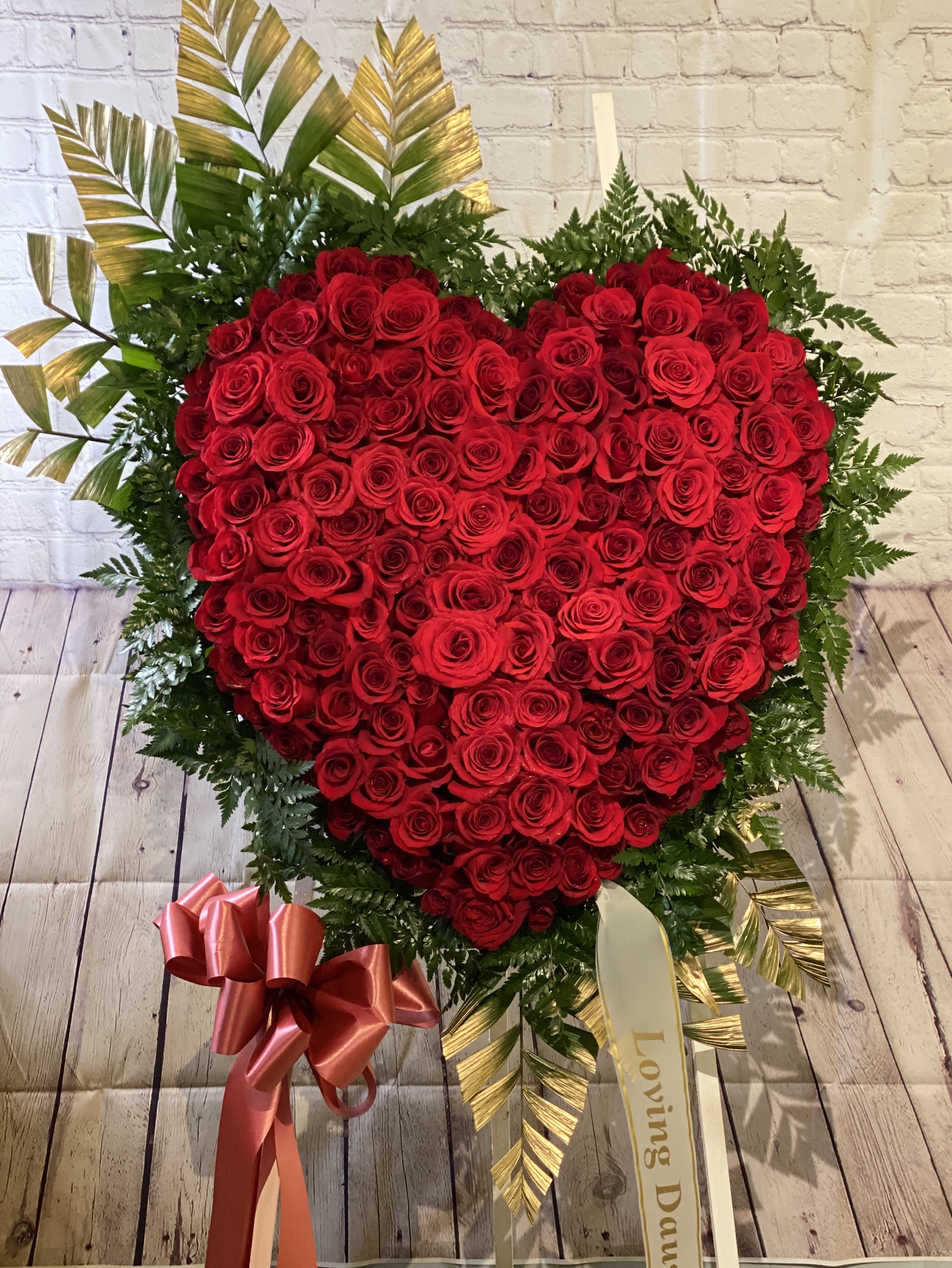 Heart-shaped red rose arrangement with ribbon and greenery