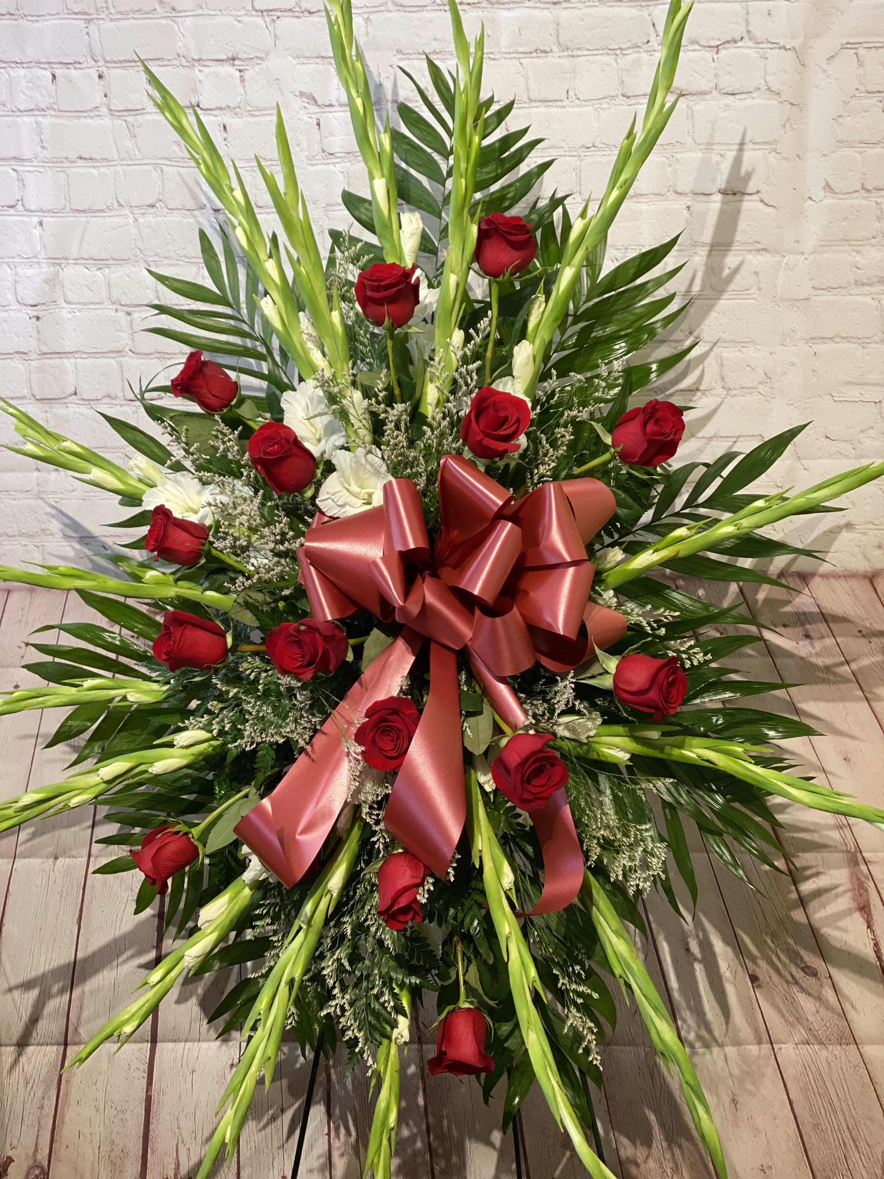 Standing floral spray of red roses with a large pink ribbon