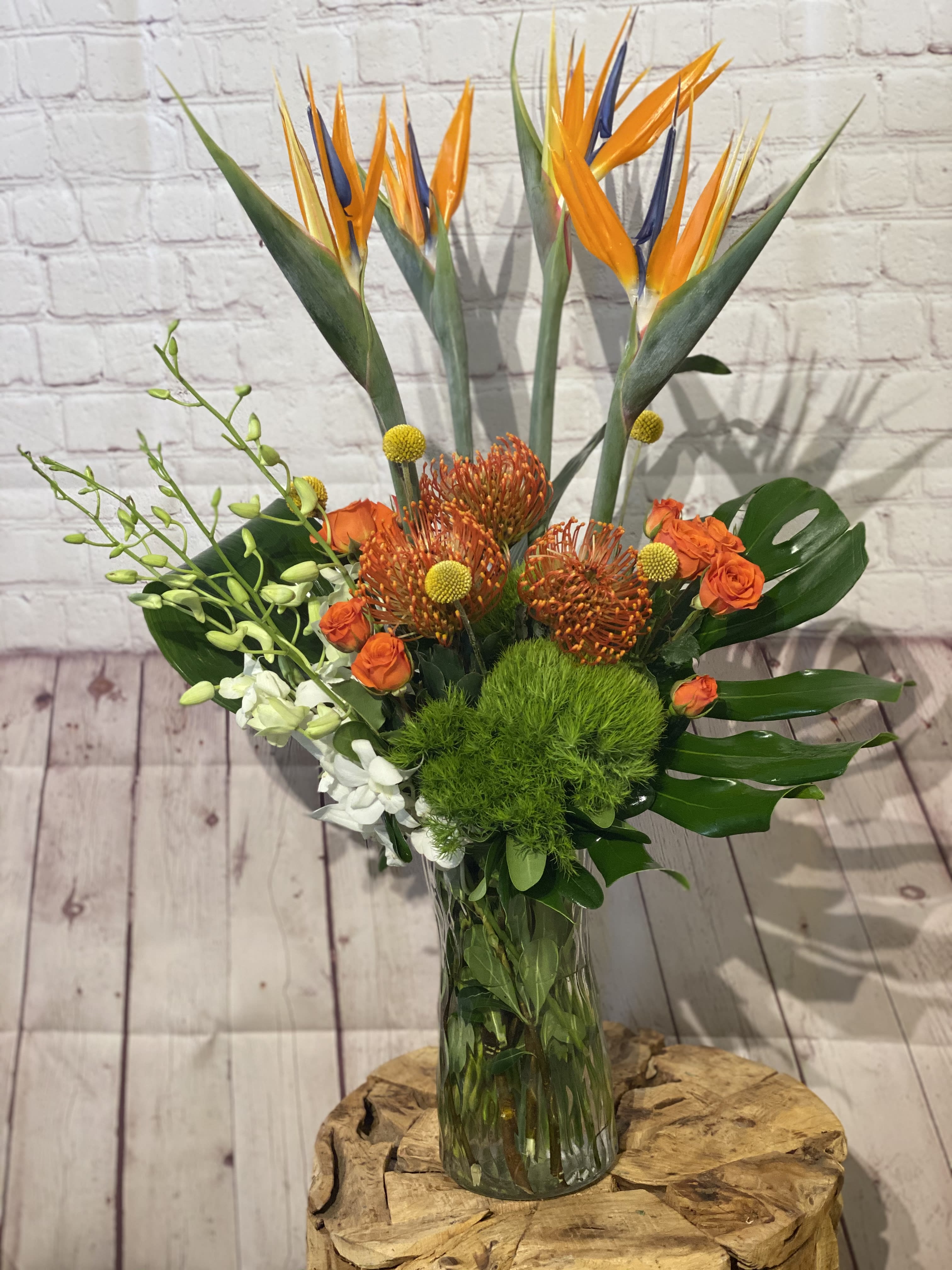 Tropical bouquet with bird of paradise, orange roses, and green filler in a glass vase