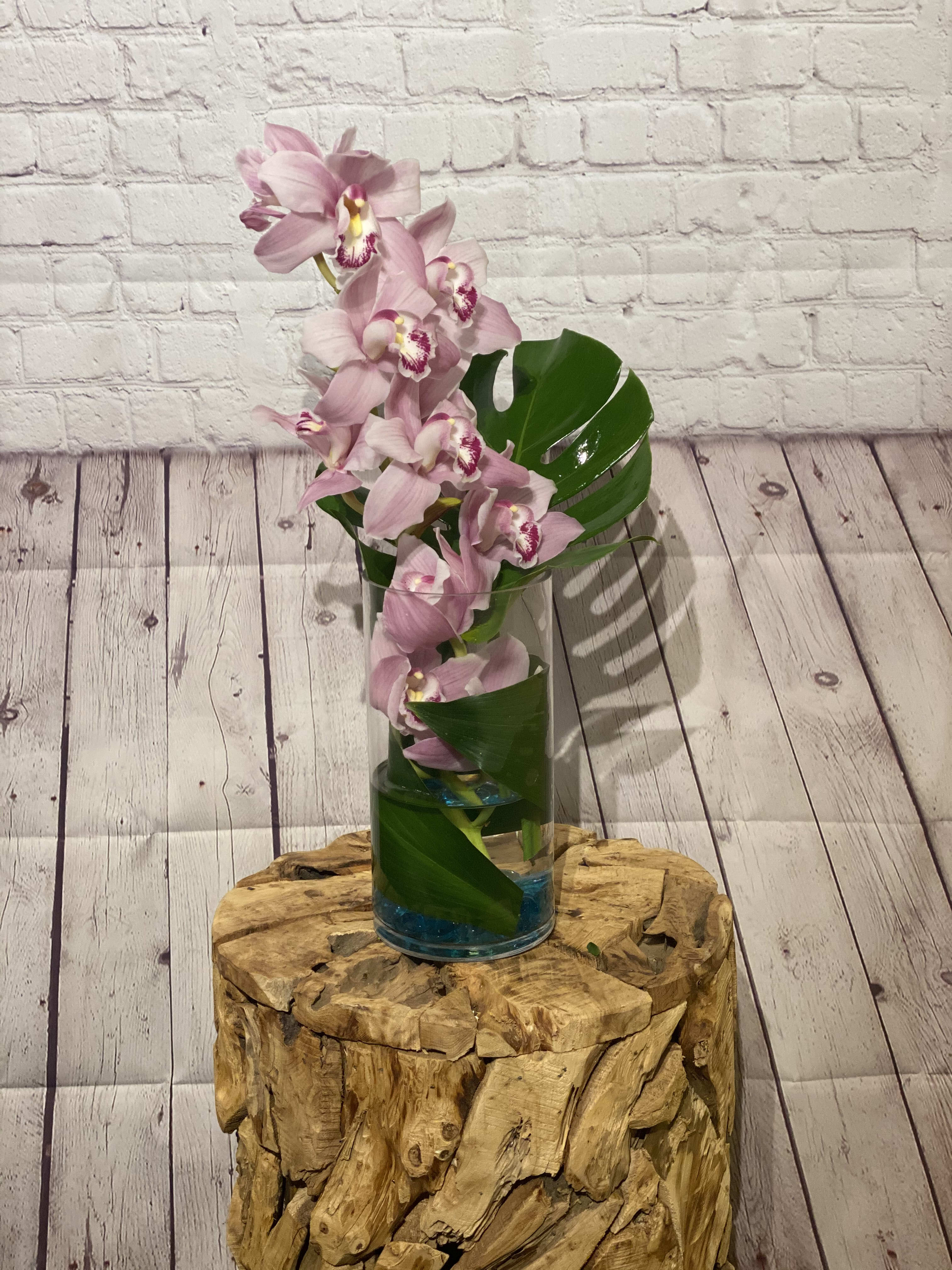 Pink orchids arranged in a clear glass vase with broad green leaves.