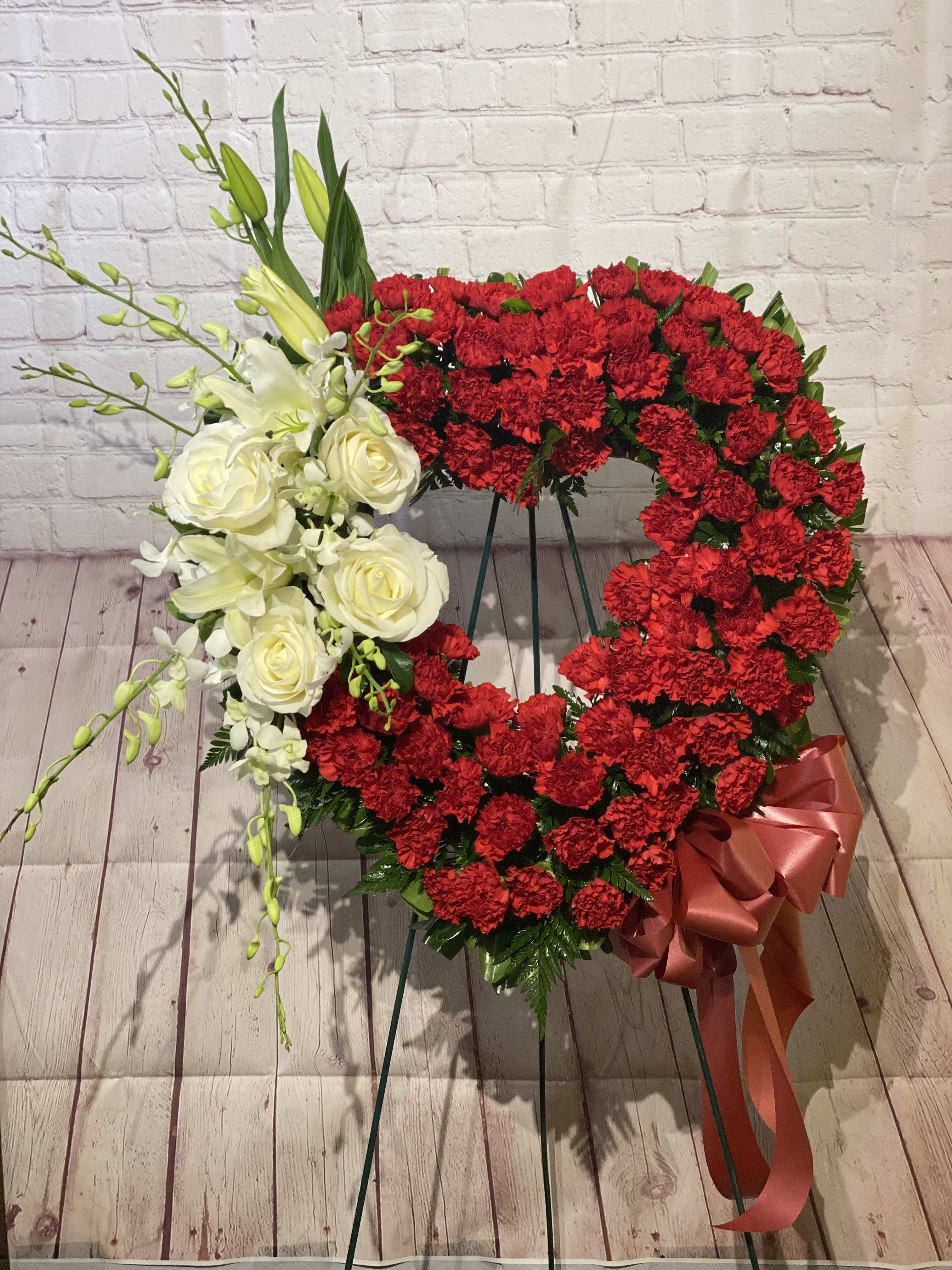 Heart-shaped floral wreath with red carnations and white roses on an easel
