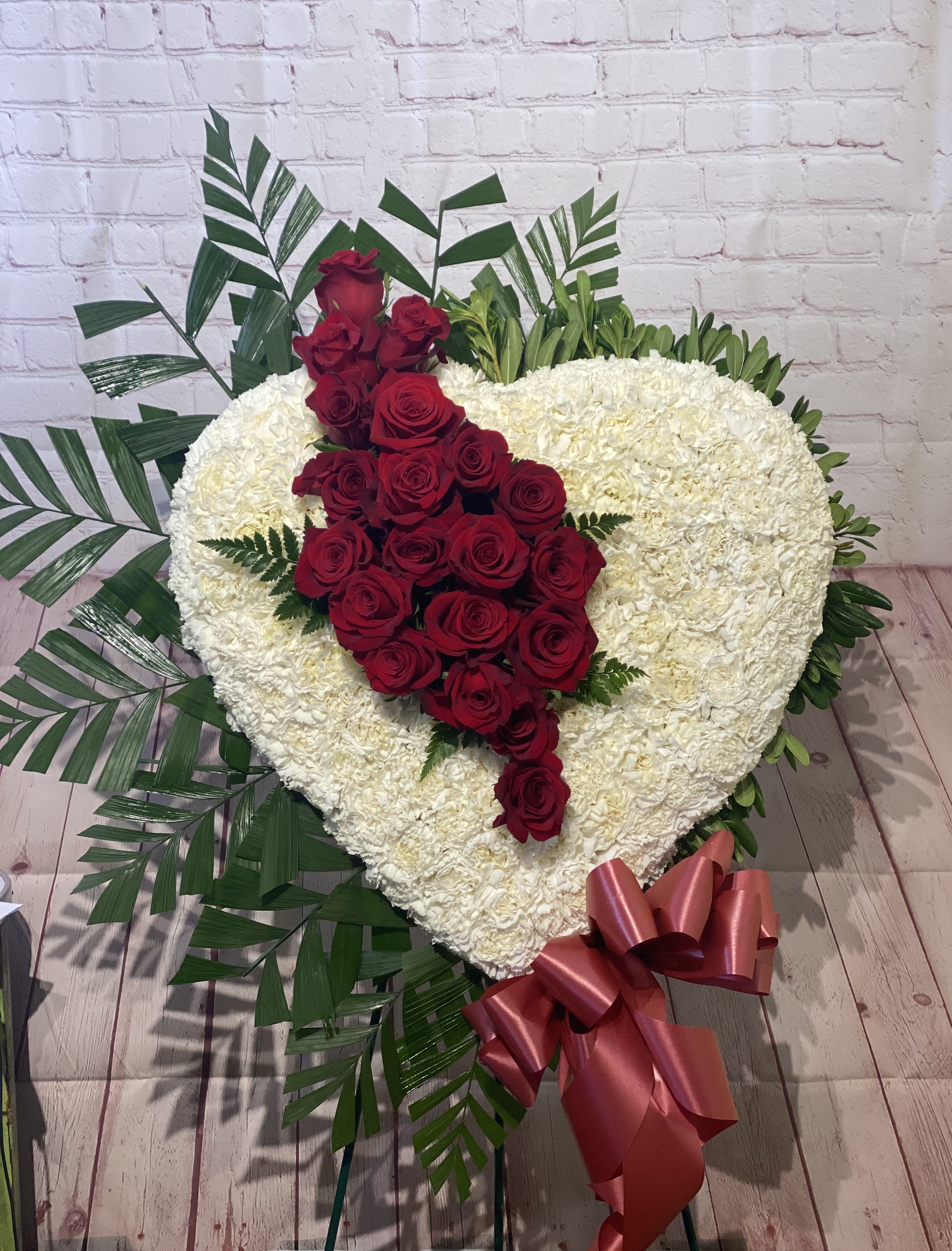 Heart-shaped white floral arrangement with red roses and a pink ribbon bow