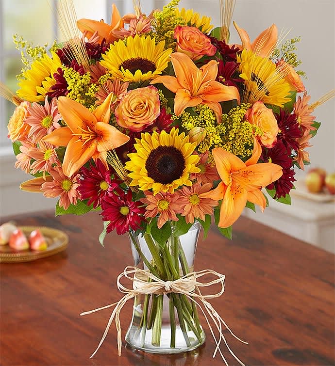 Bouquet of sunflowers, orange lilies, and roses in a glass vase