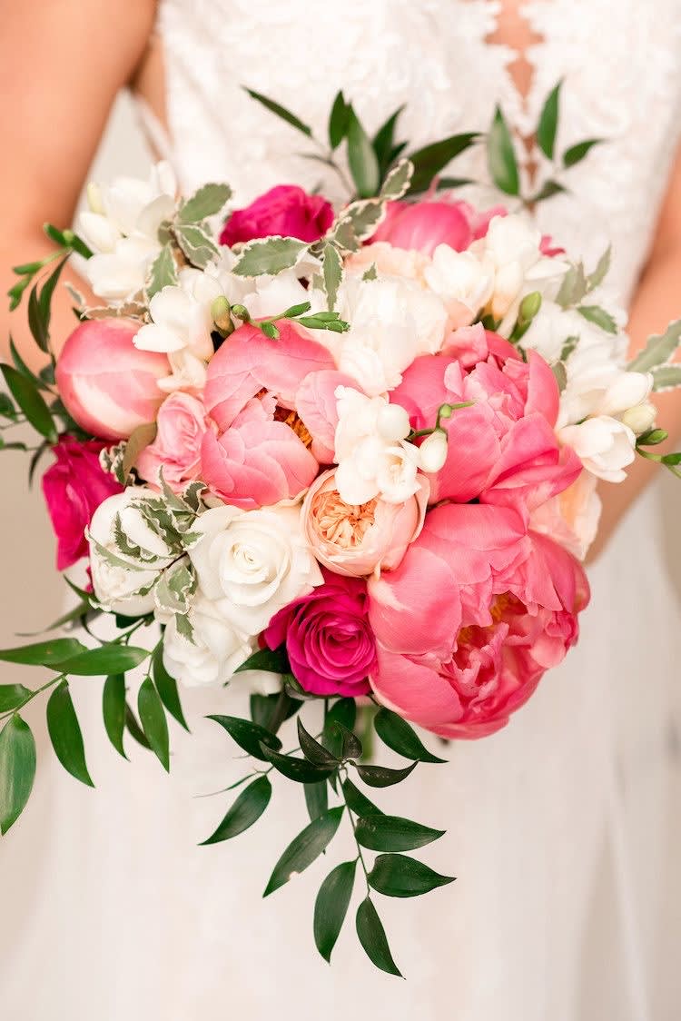 Handheld bouquet of pink and white flowers with trailing greenery