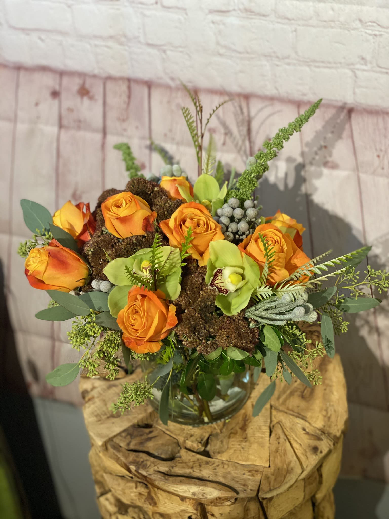 Orange roses and green orchids arranged in a glass vase