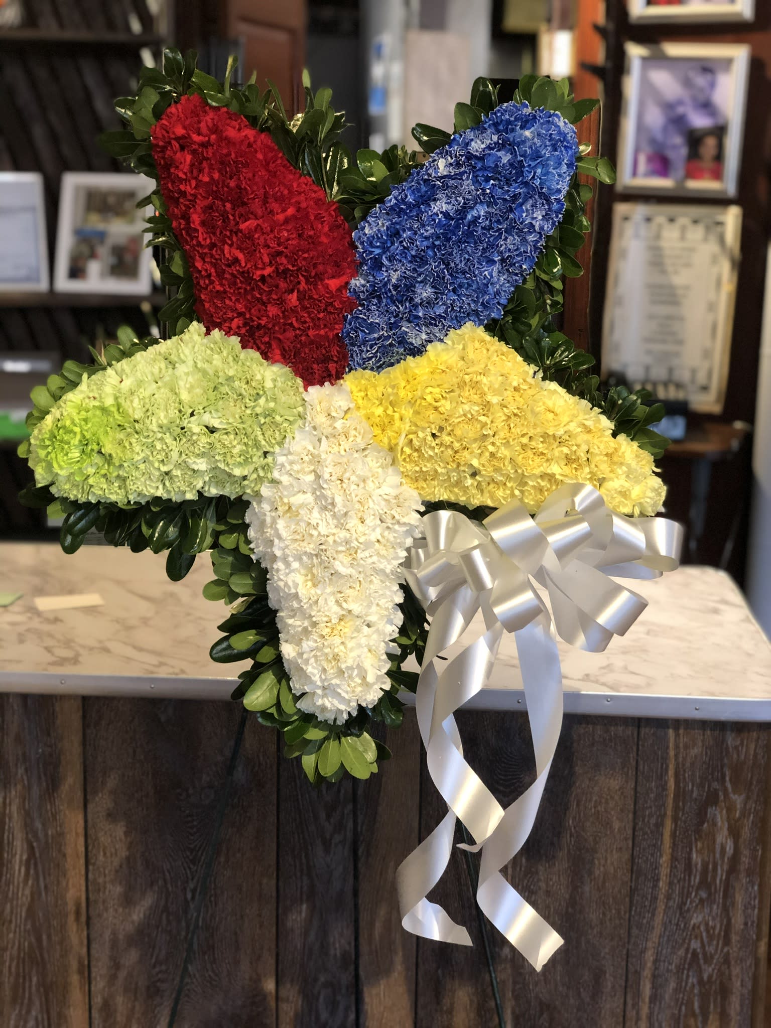 Cross-shaped floral tribute with red, blue, yellow, green, and white flowers