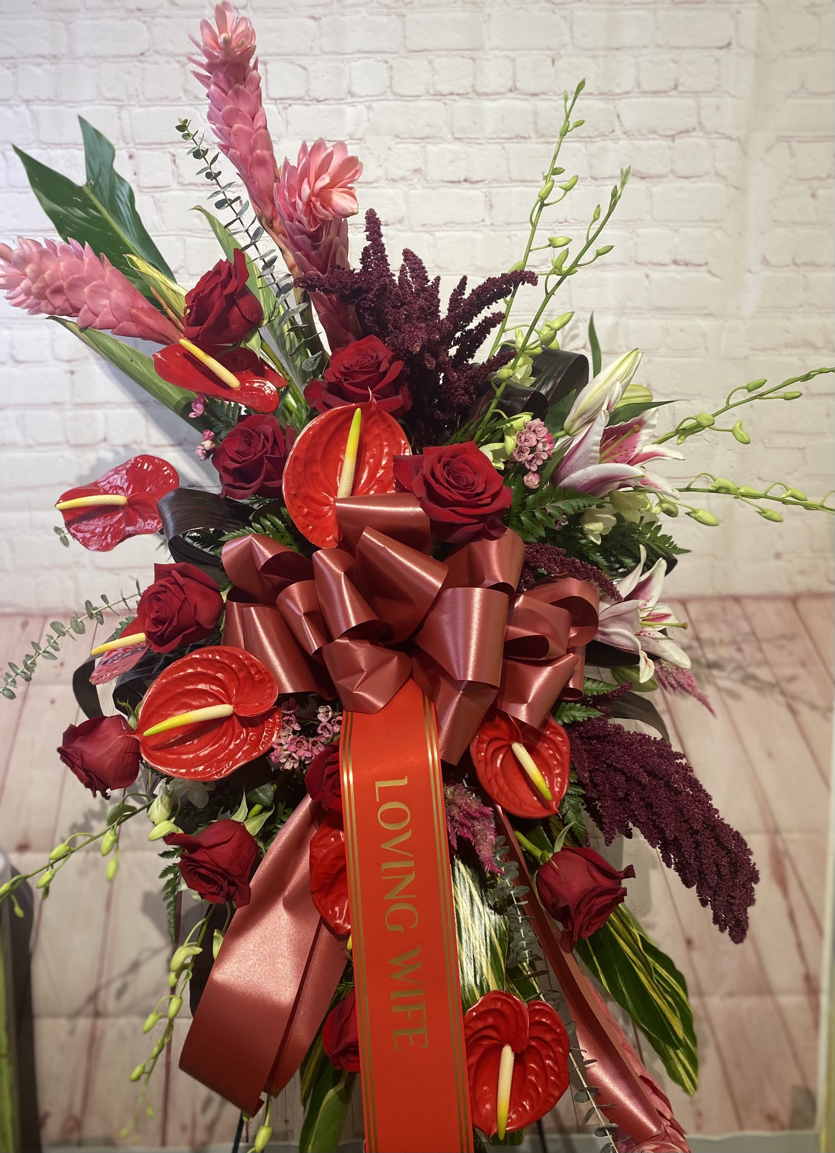 Red roses and tropical flowers arranged with a large ribbon bow