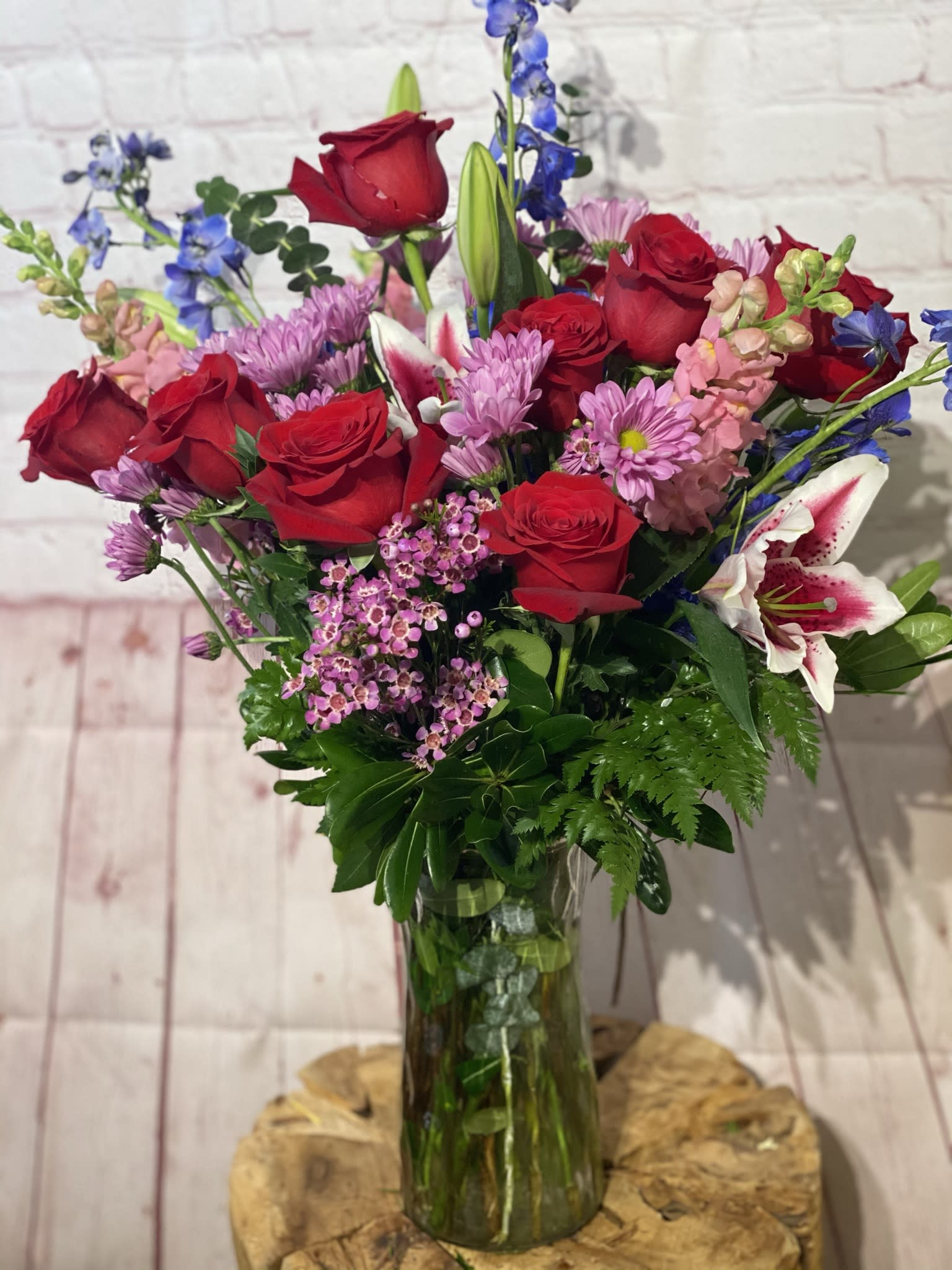 Bouquet of red roses, pink lilies, and purple flowers in a glass vase