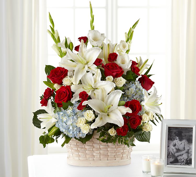 Basket arrangement of red roses, white lilies, and blue hydrangeas