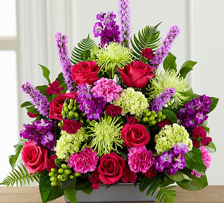 Mixed bouquet of pink roses, purple blooms, and green flowers in a rectangular vase