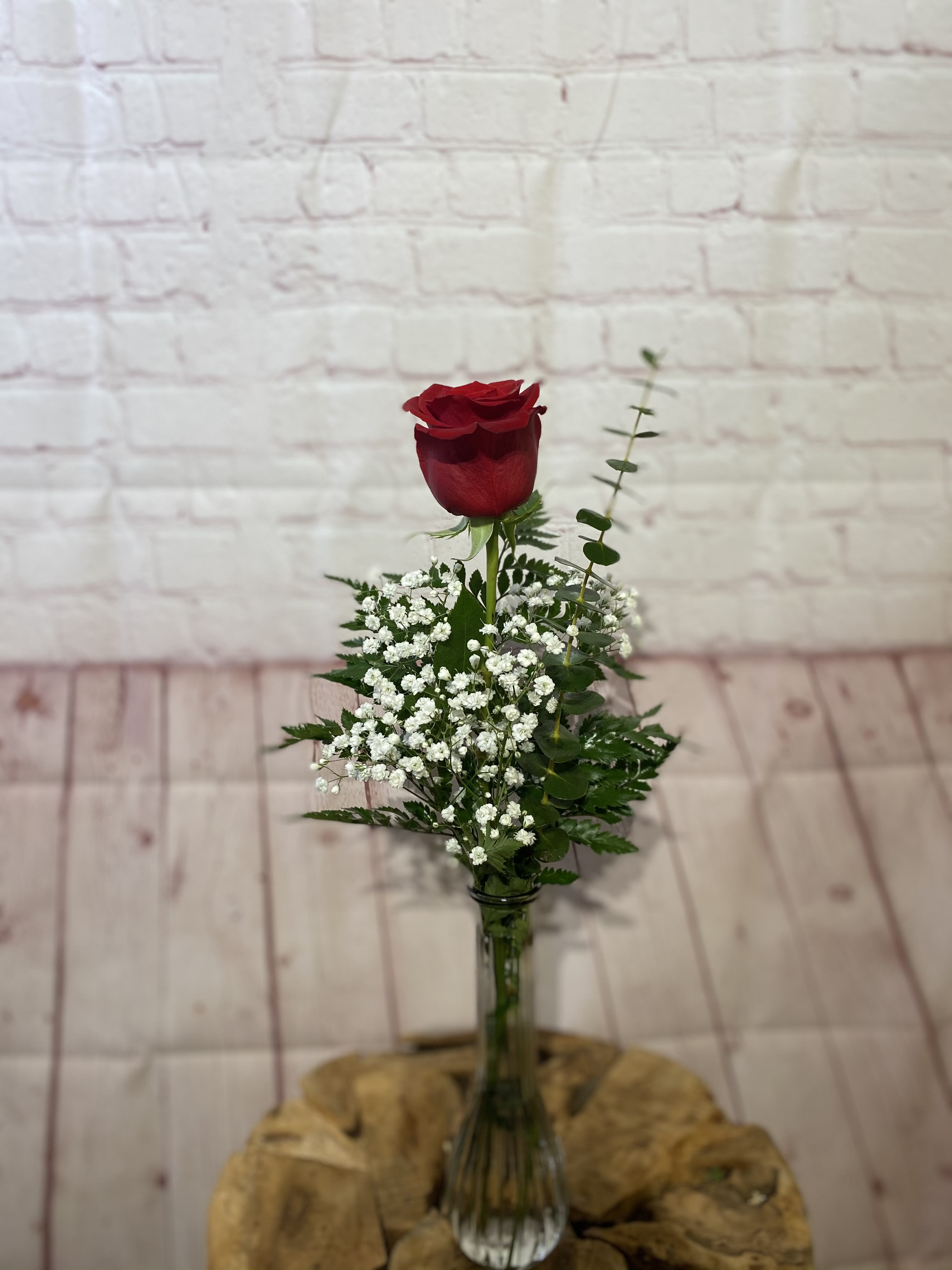 Single red rose in a clear glass vase with white filler flowers