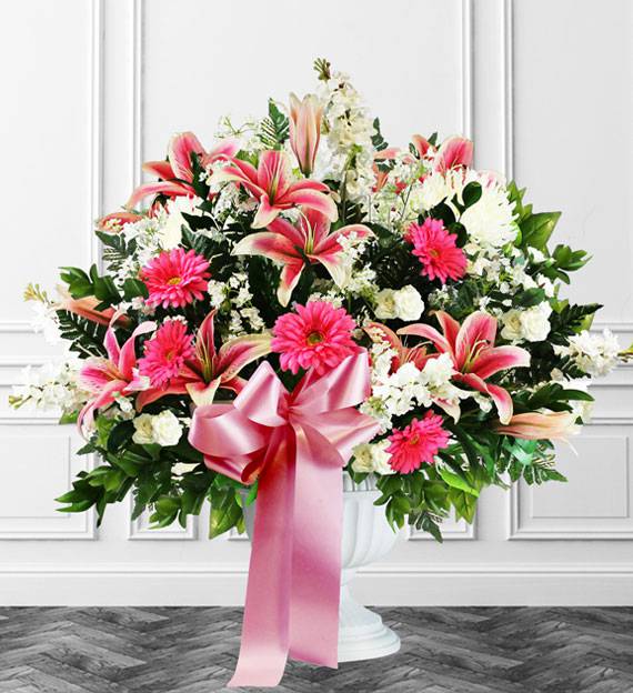 Pink lilies and daisies in a white pedestal vase with a pink ribbon